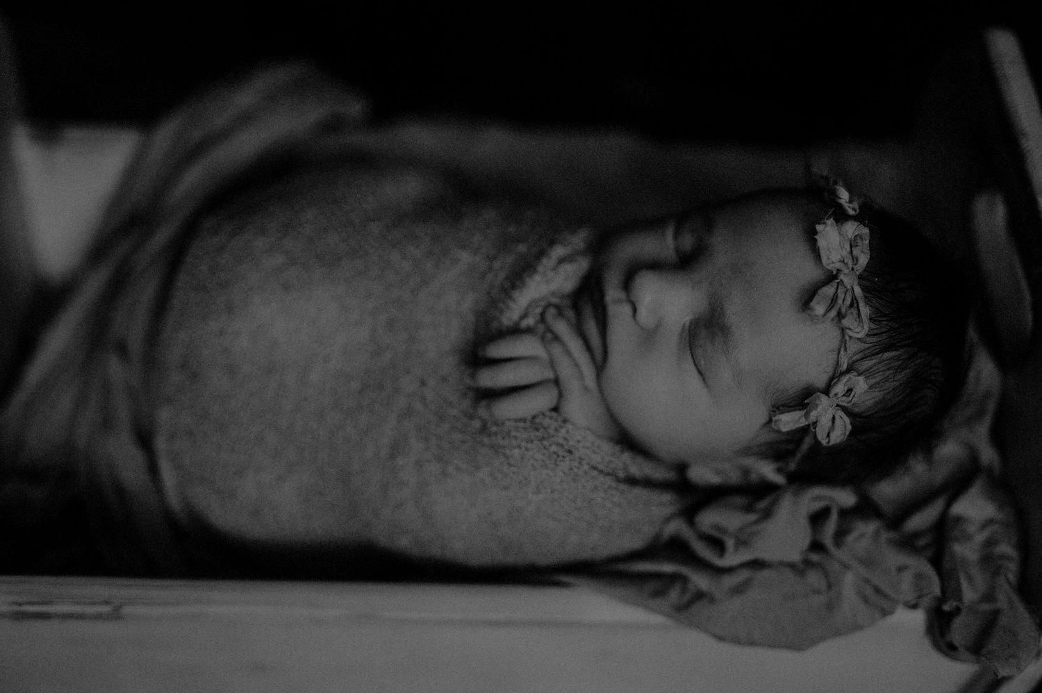 A black and white portrait of a sleeping baby adorned with a small floral headband.