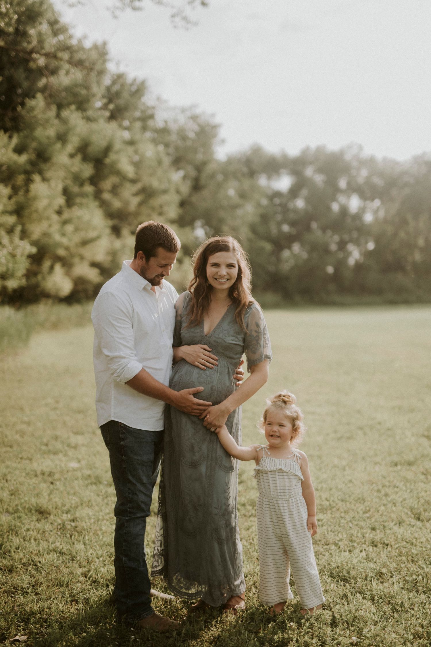 A family shares tender moments in a sunlit meadow wearing casual attire during a maternity photo session.