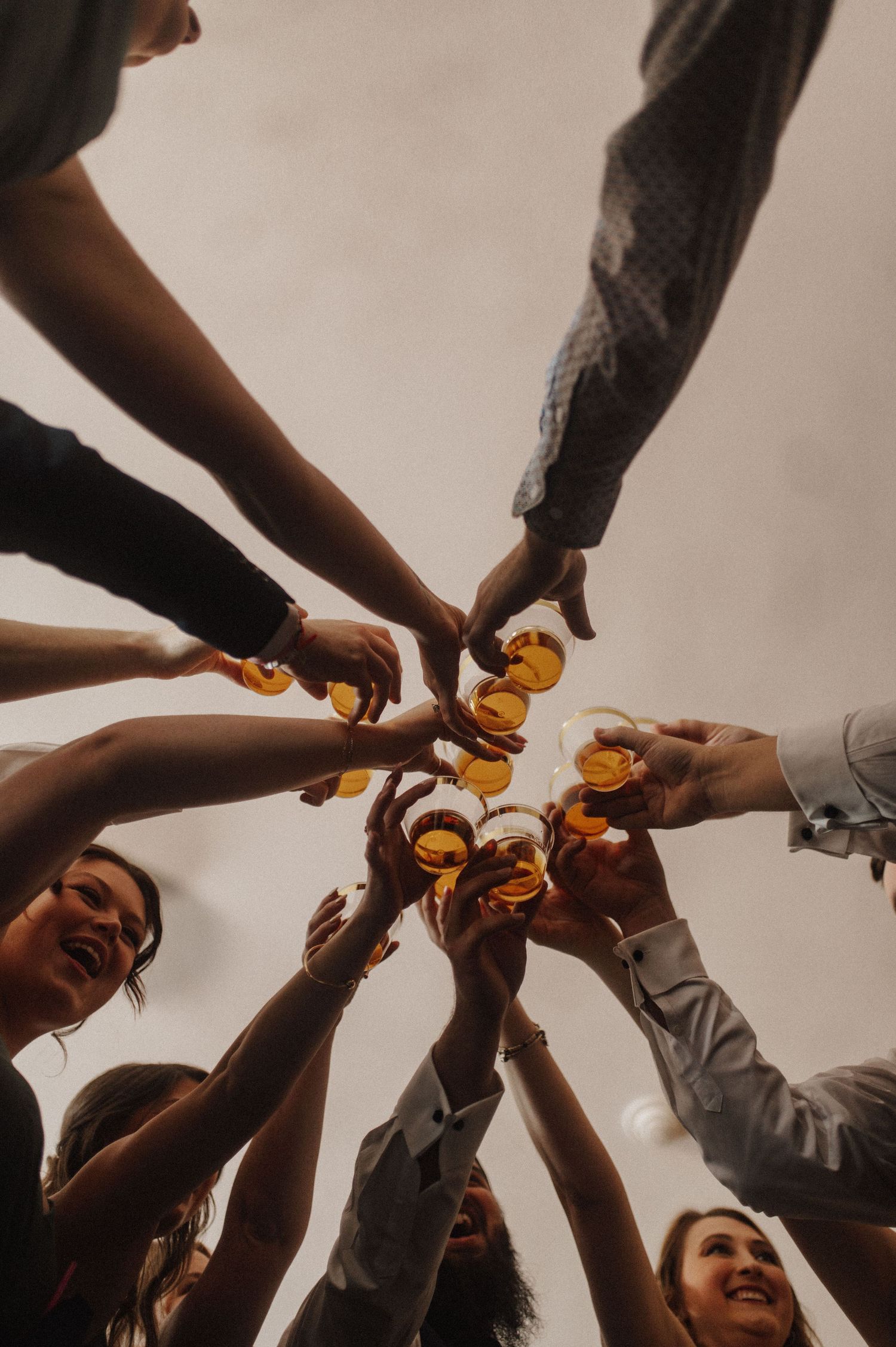 Group of friends toasting with amber-colored drinks in glass bottles at a celebratory gathering.