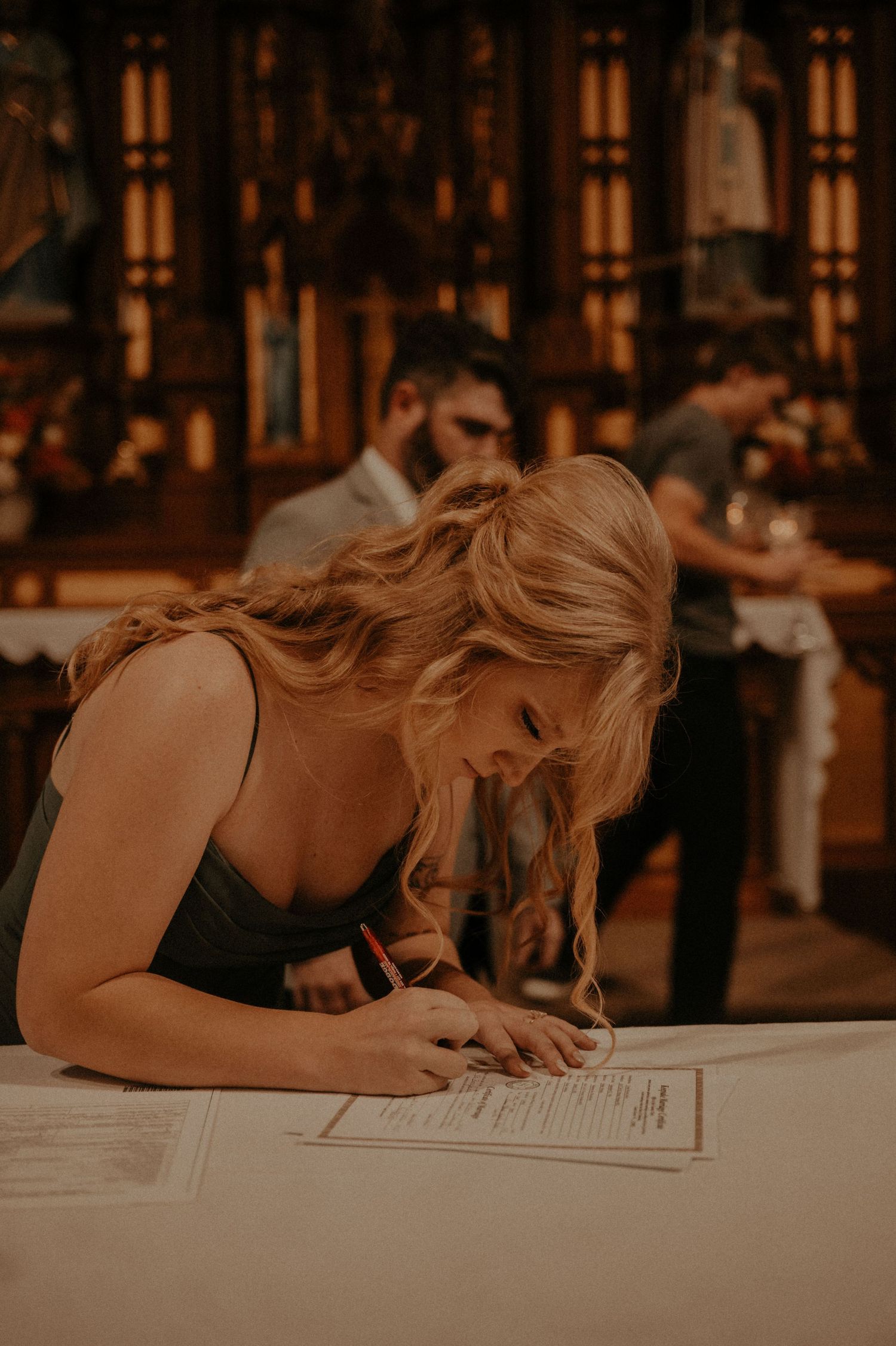 Person signing documents at a table in a dimly lit church interior.