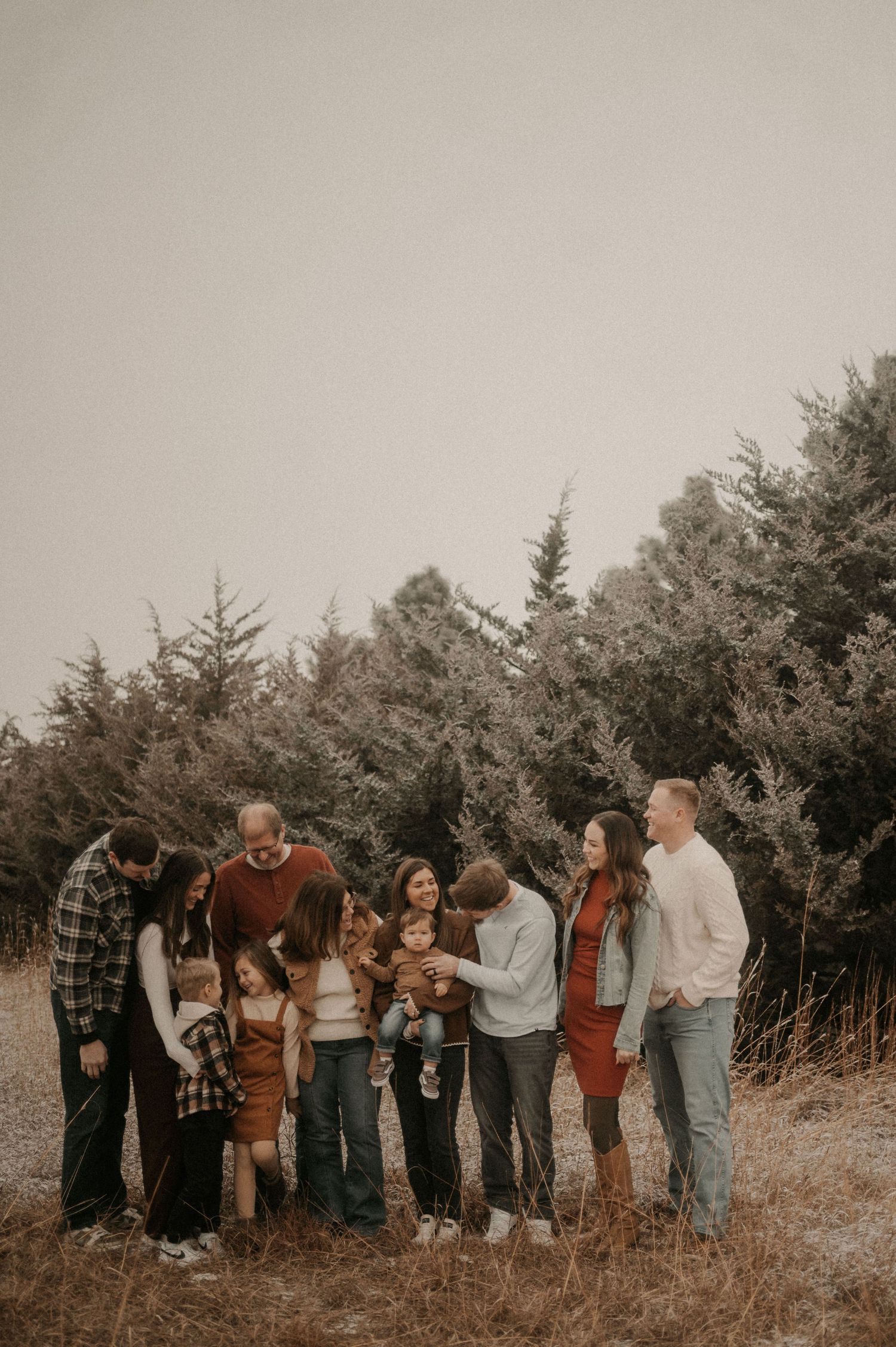A group of people standing together on a hillside against a backdrop of evergreen trees in muted earth tones.