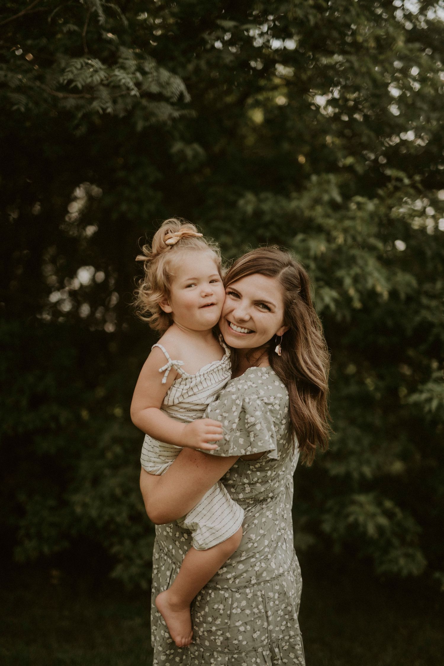 A tender moment of affection and laughter shared between parent and child against a lush green outdoor backdrop.