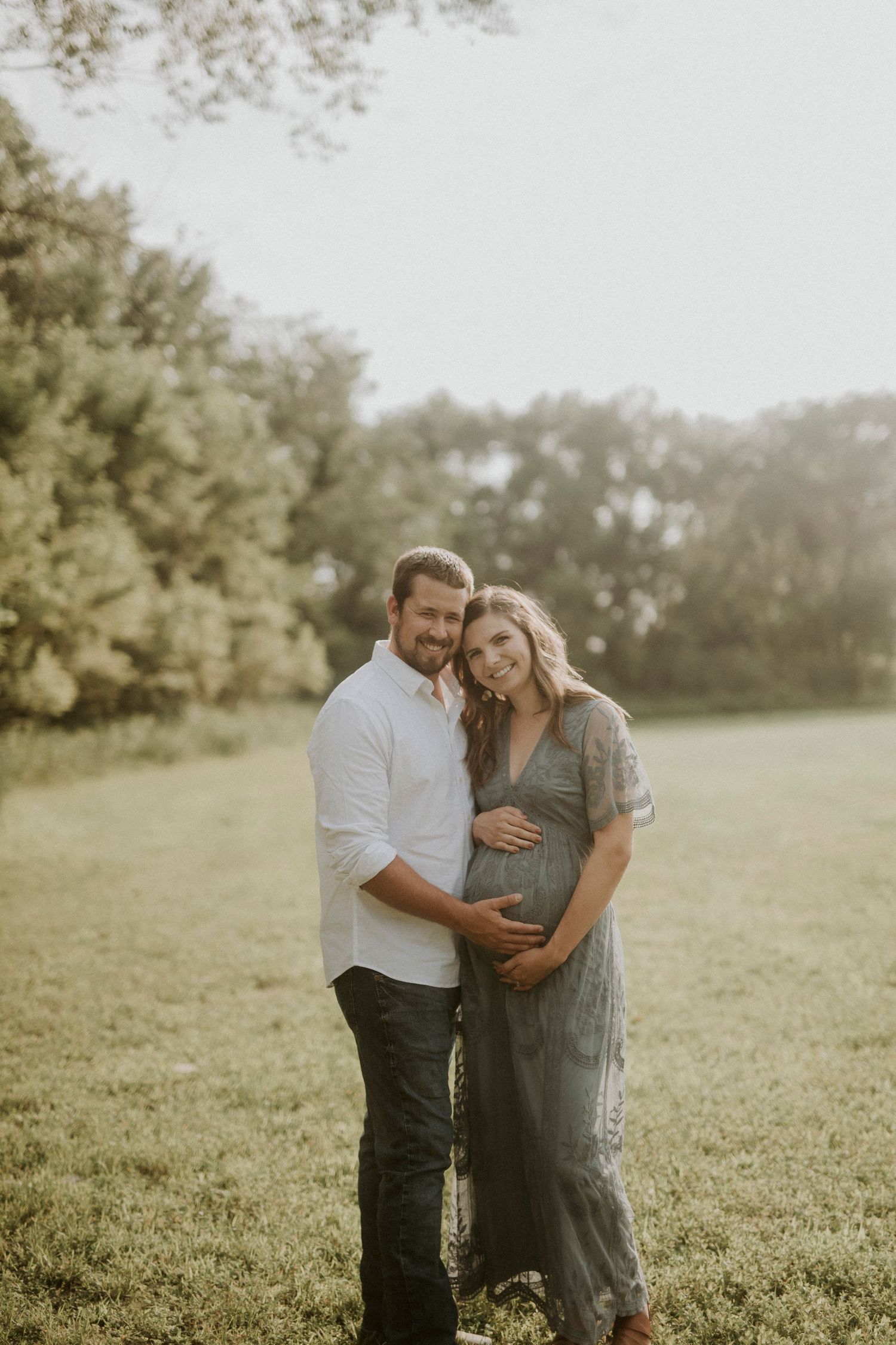 A couple embraces in a sunlit meadow wearing casual attire during an outdoor photo session.
