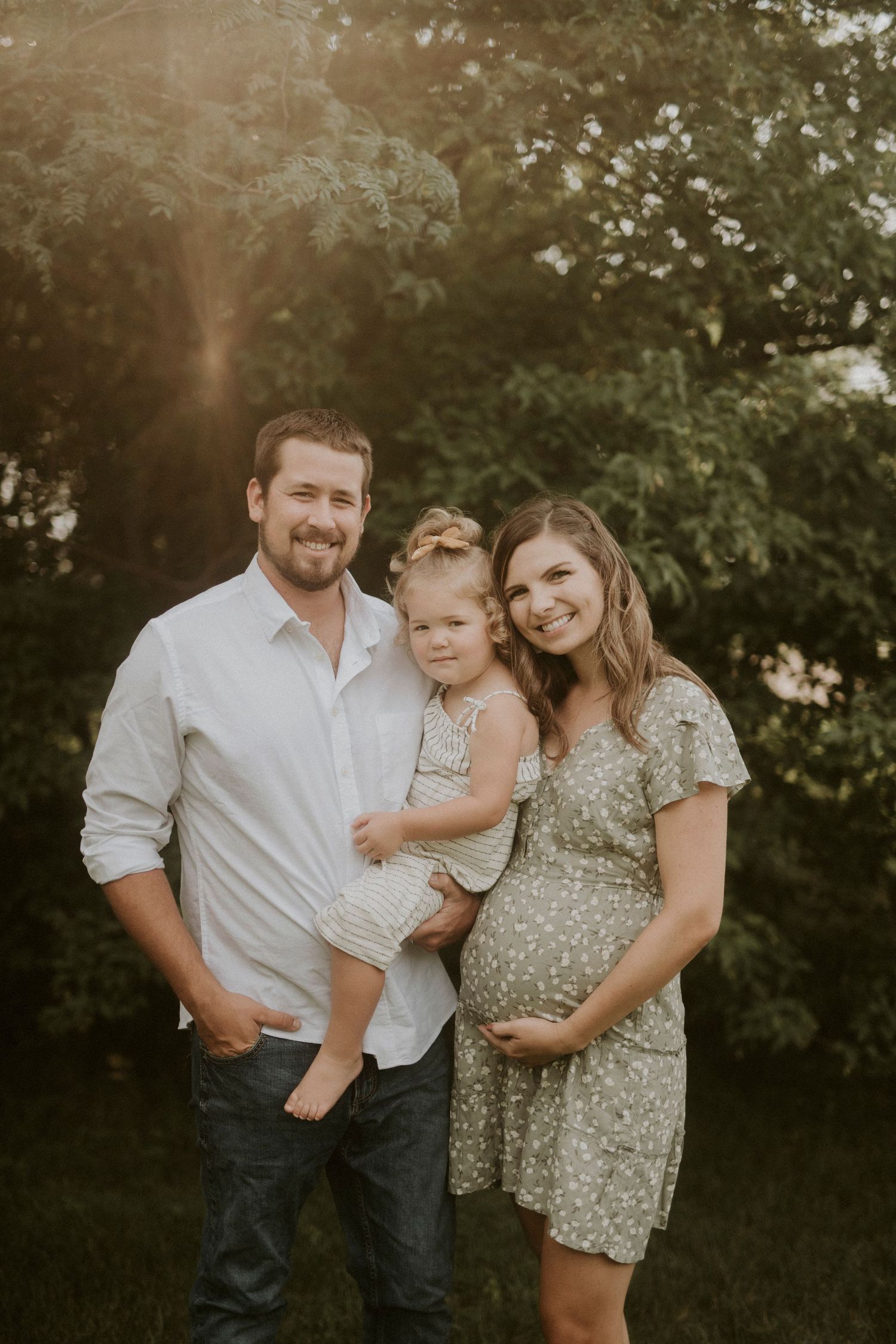 A family of three poses together outdoors during golden hour in a natural garden setting.