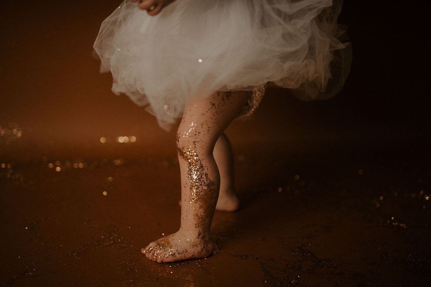 A person's bare feet in a white dress step through water creating ripples in a dark moody setting.