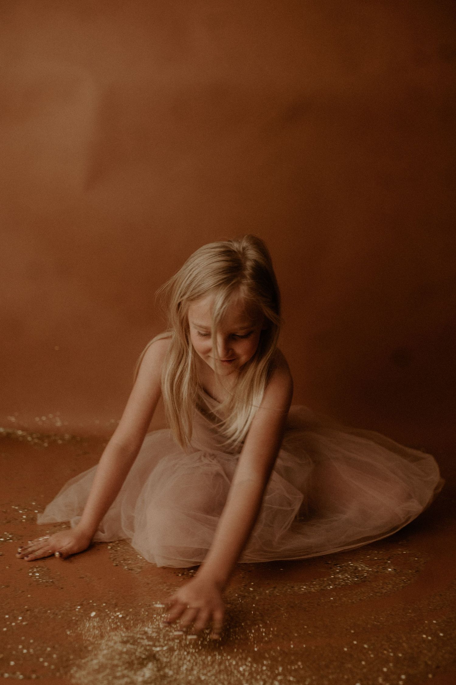 A series of sepia-toned photos shows a person in a flowing dress lying on the floor gathering scattered glitter.