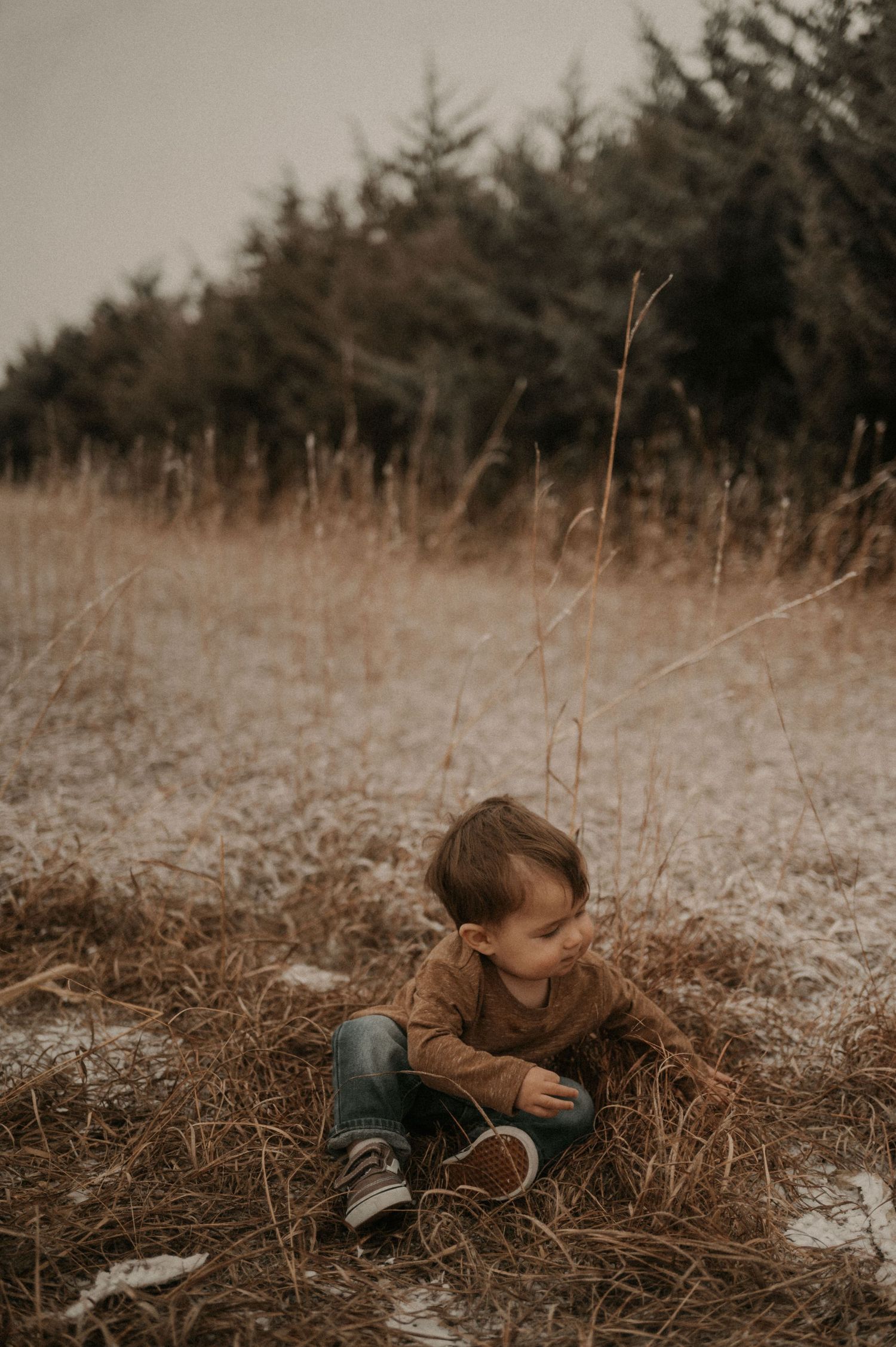 A child lies peacefully in a field of dried grass and fallen leaves on an autumn day.