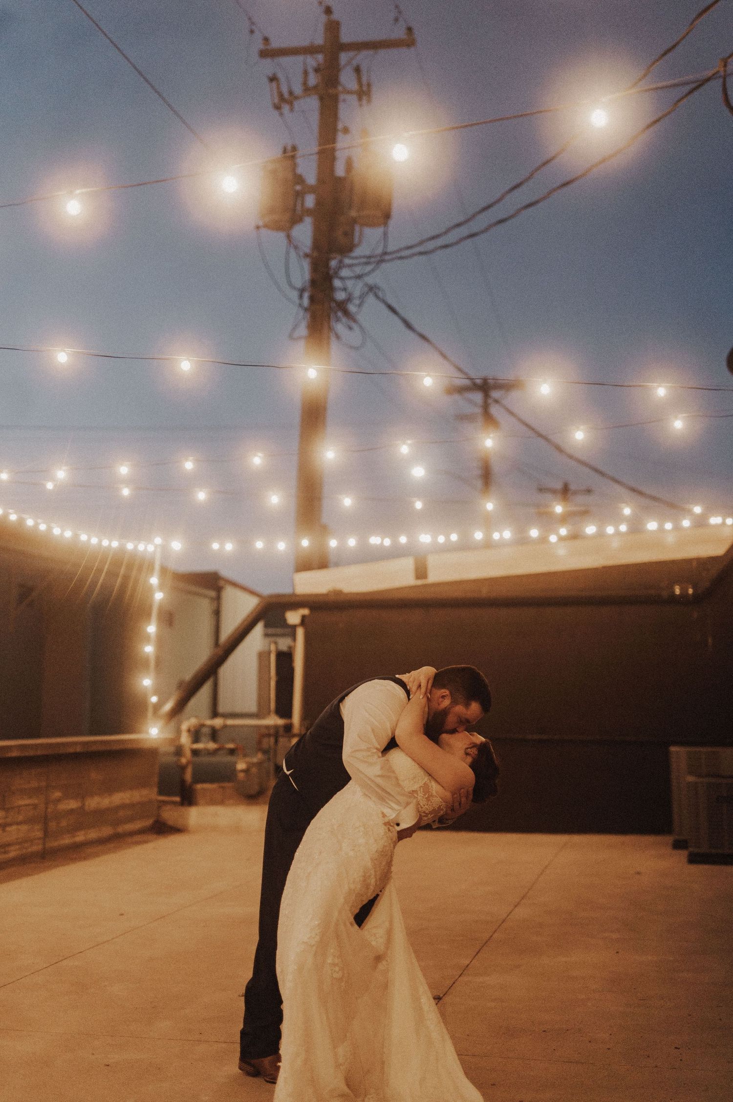 Couple sharing an intimate dance moment under outdoor string lights at twilight.