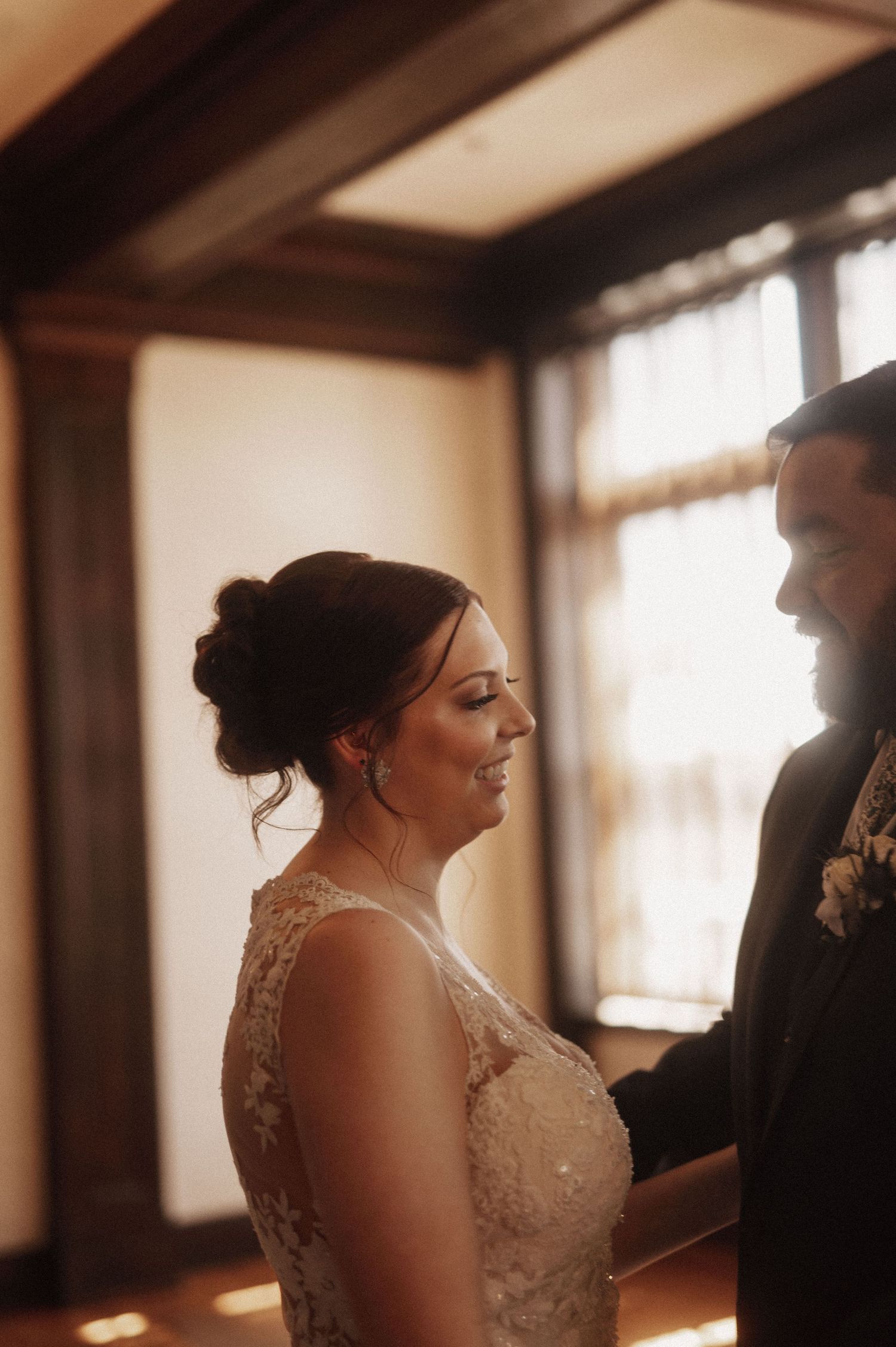 A warm-toned wedding photo showing an intimate moment between two people in formal attire.