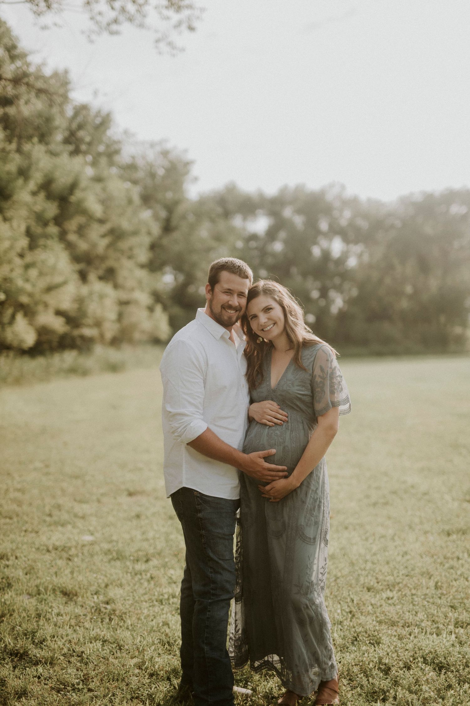 A couple shares an intimate moment in a sunlit field during a maternity photoshoot.