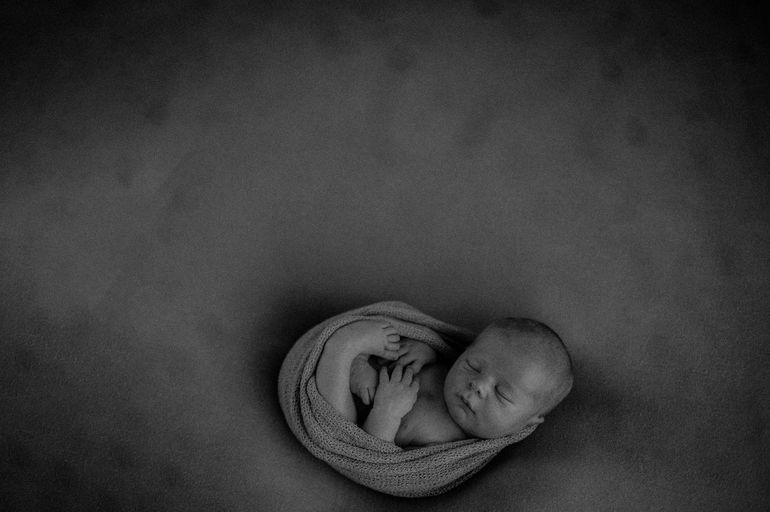 A sleeping newborn baby curled up in a peaceful fetal position, captured in black and white photography.