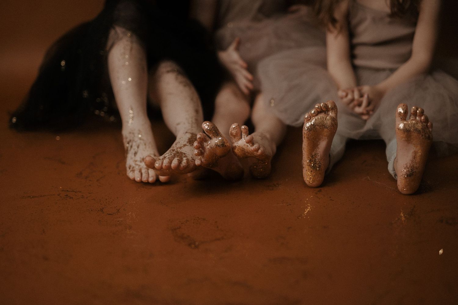 Feet of multiple people sitting together on a brown floor in a casual gathering.