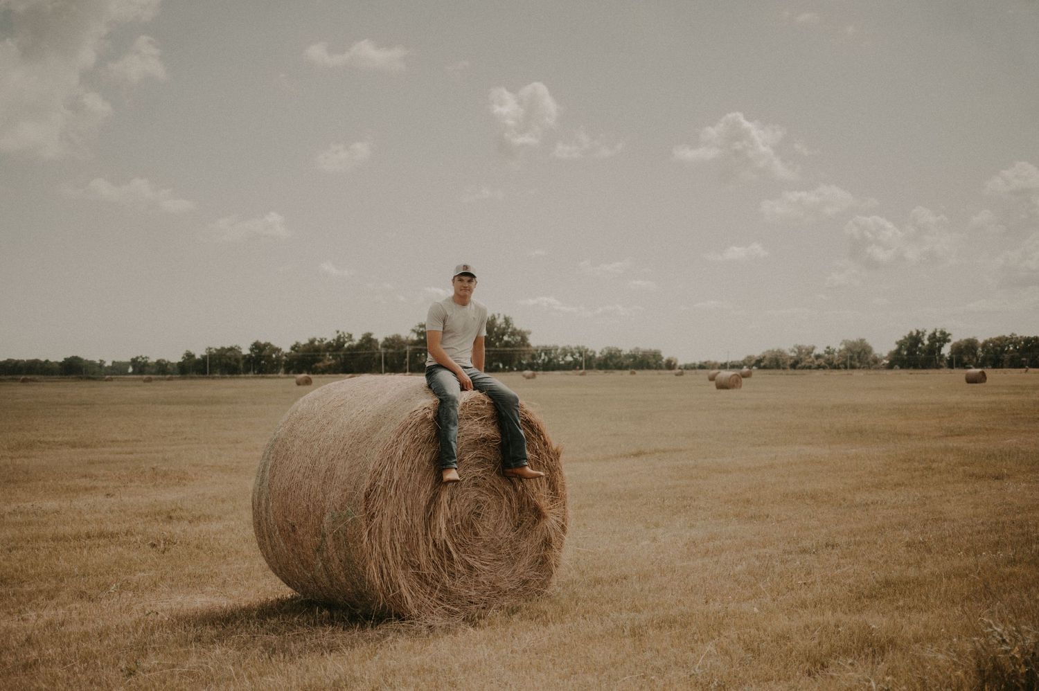 Round hay bales dot a golden wheat field under a cloudy summer sky.