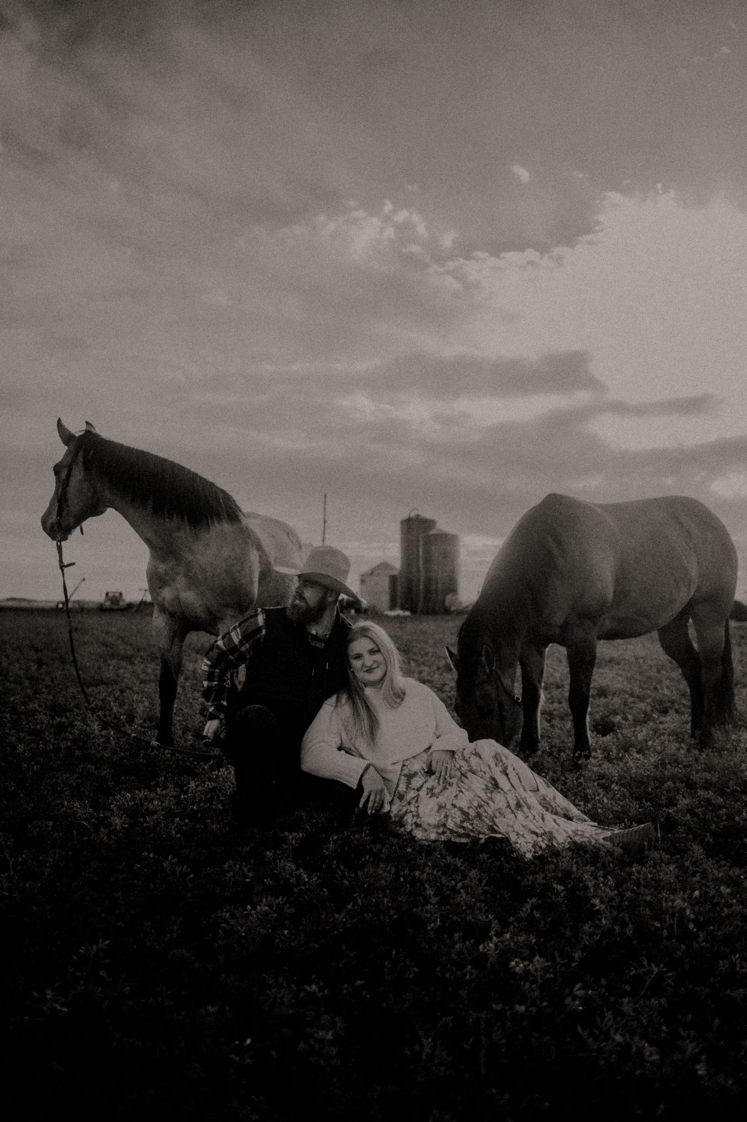 Black and white photo of horses and wedding party in a field with dramatic sky.