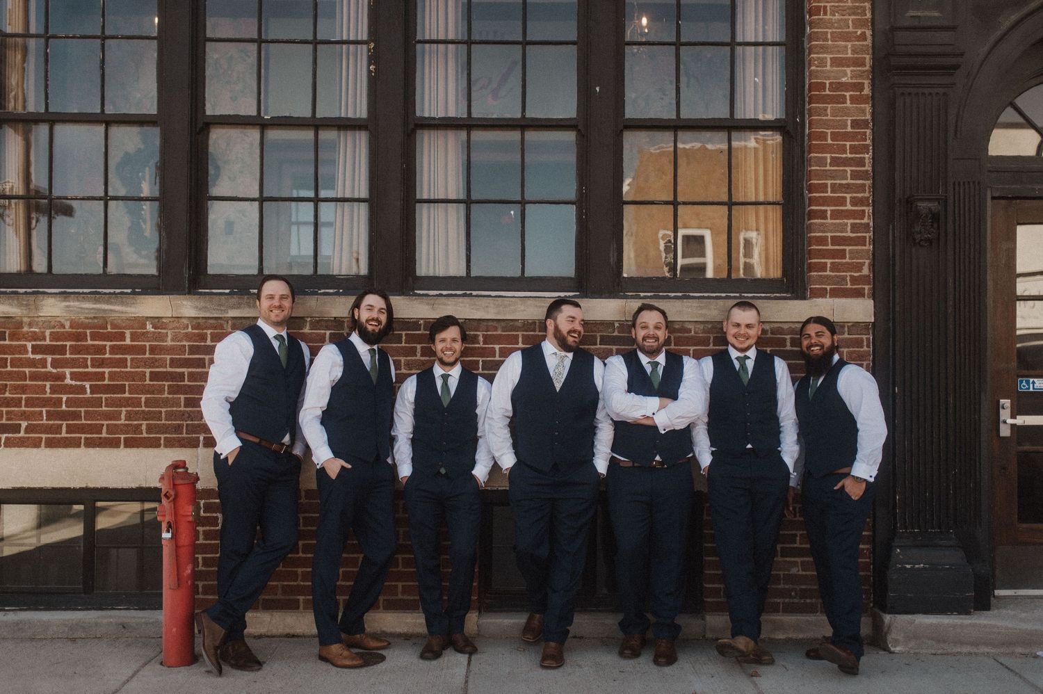 Wedding party in formal attire posed against industrial brick backdrop.