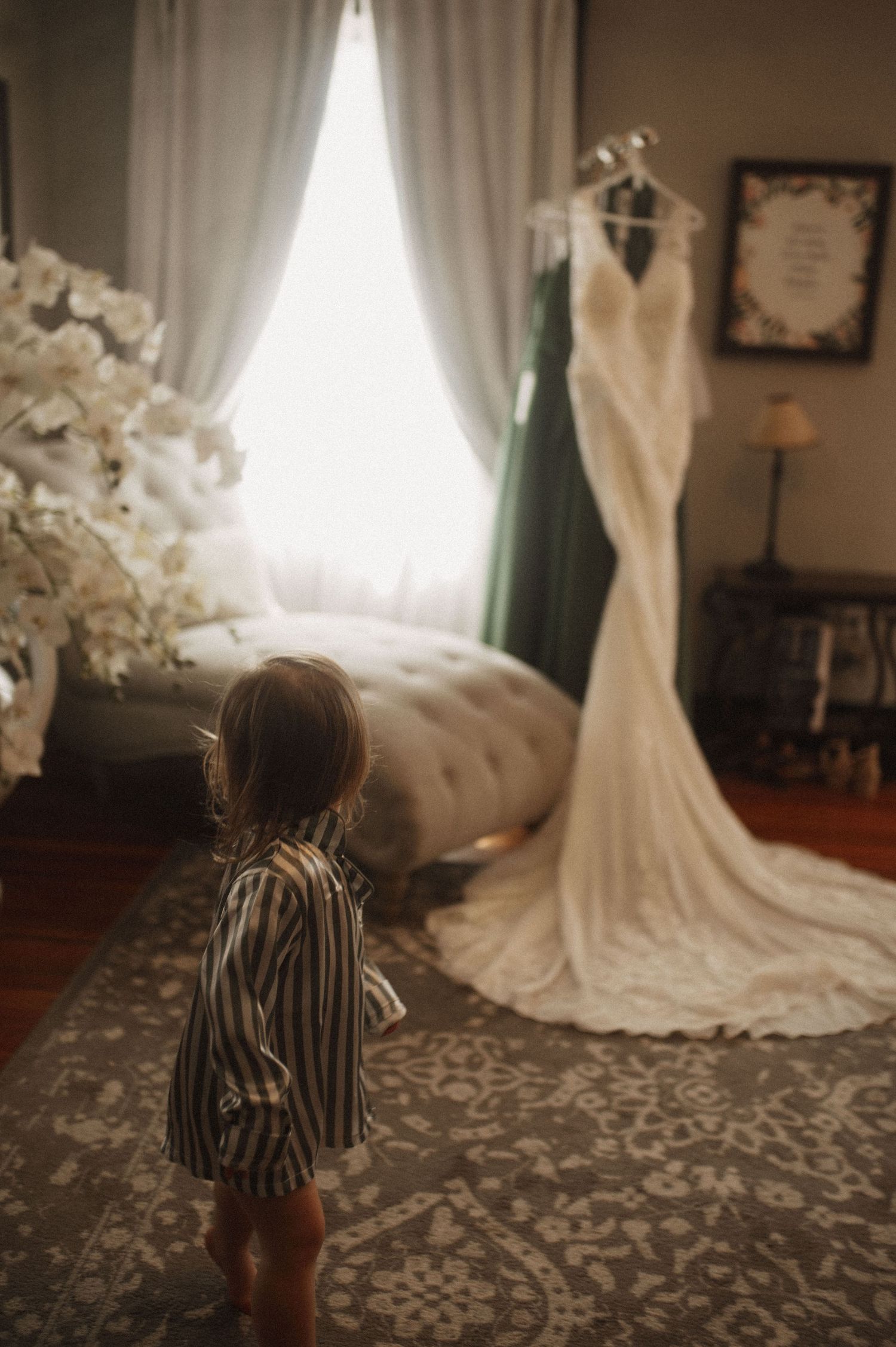 Wedding dress on display in a sunlit room with patterned carpet.