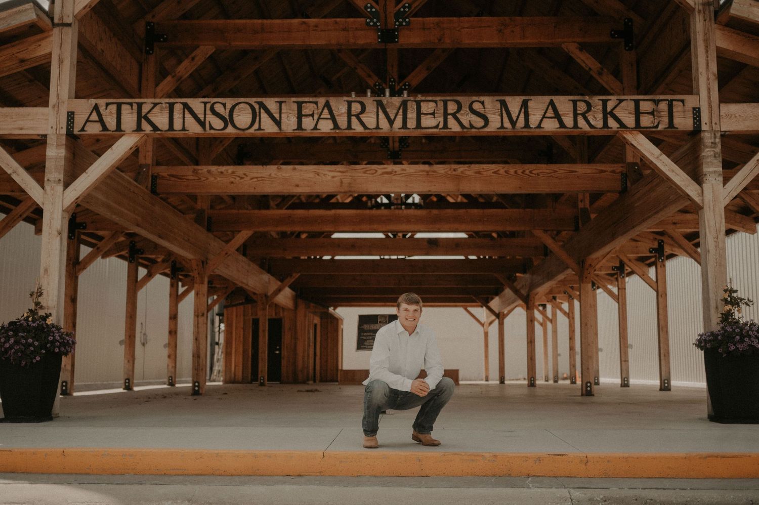 A person crouches under the rustic wooden entrance sign of Atkinson Farmers Market.