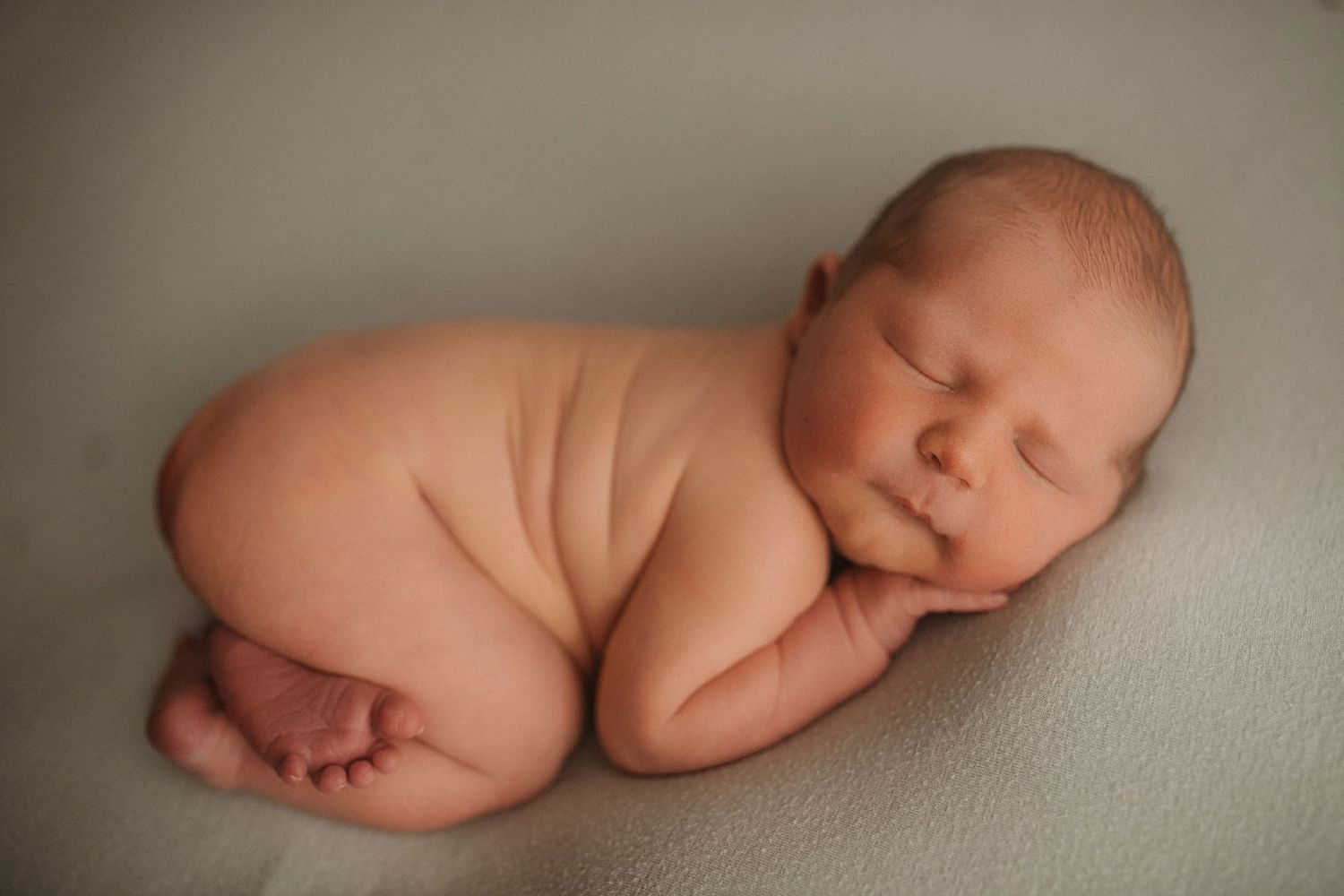 Peaceful newborn photography session showing tiny baby sleeping on soft neutral backdrop.