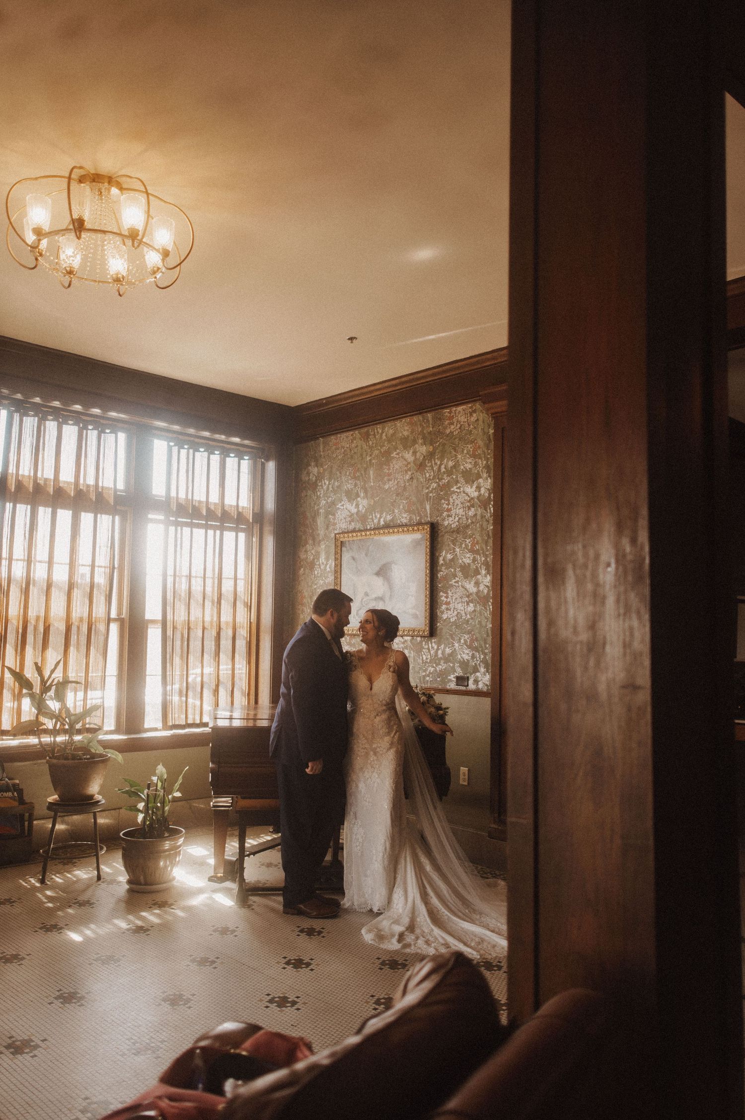 A couple shares an intimate moment in a sunlit room with vintage decor and flowing curtains.