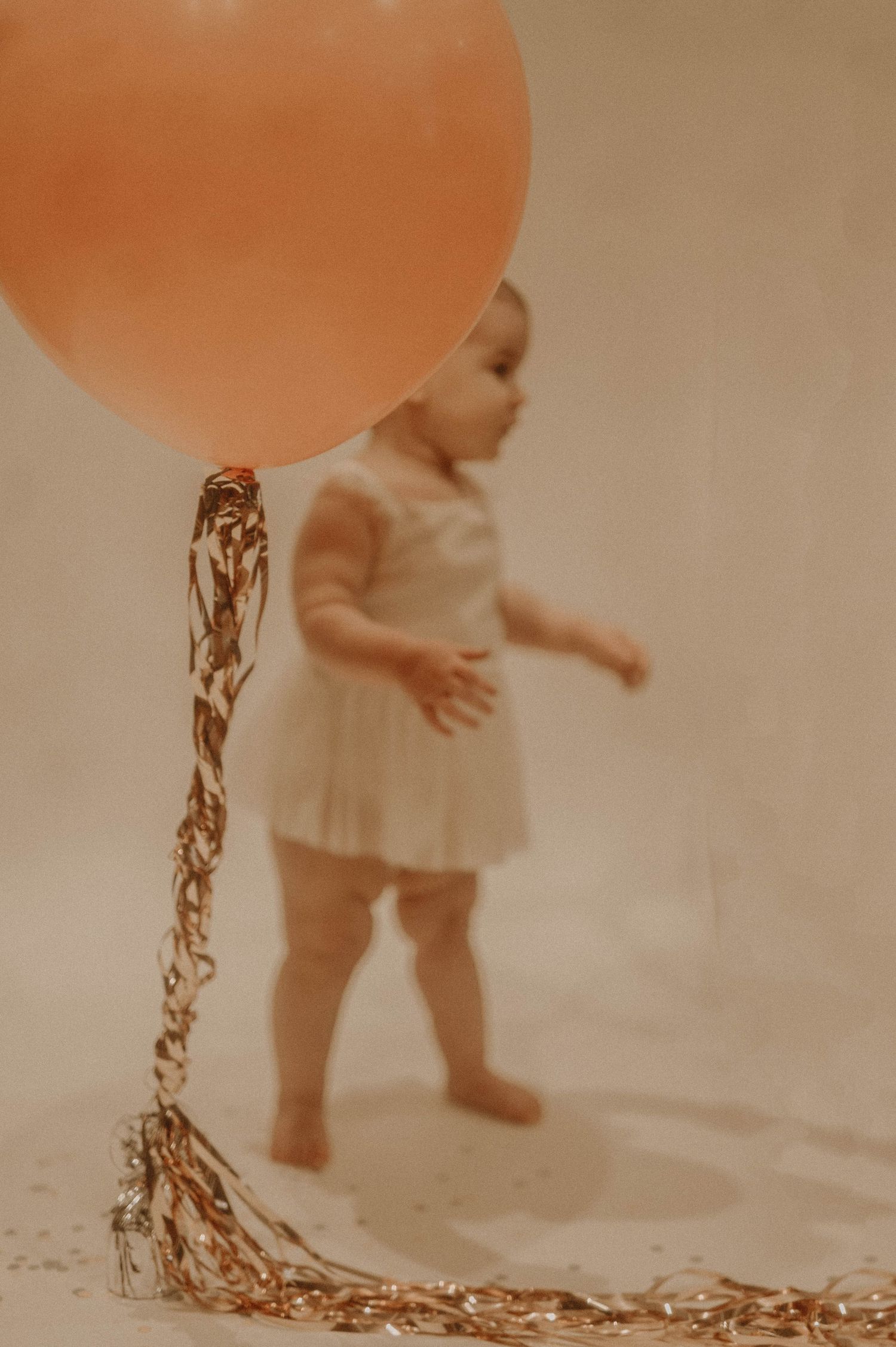 A vintage sepia-toned photograph of a small child in a dress holding a large orange balloon with sparkly streamers.