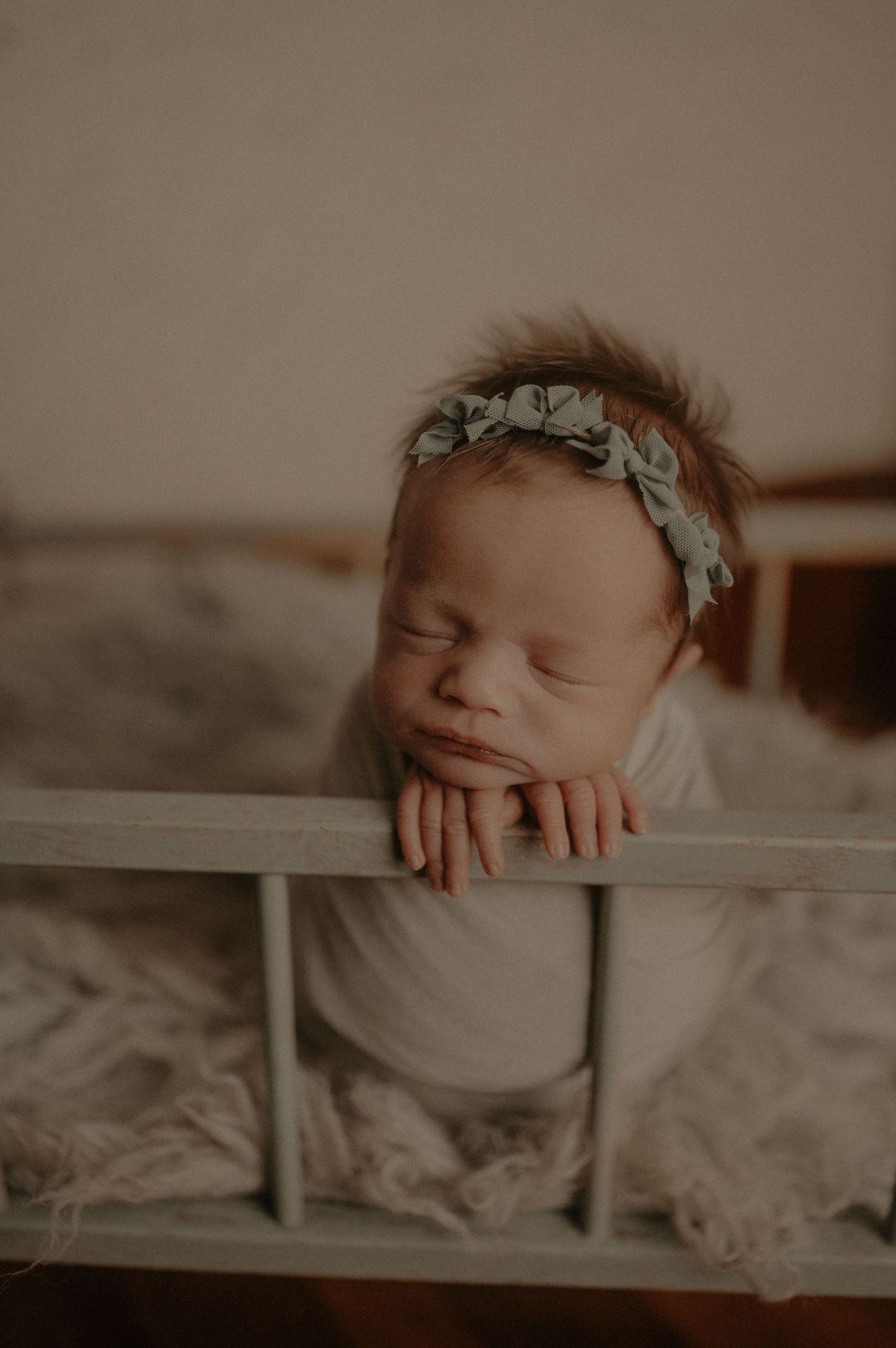 Dreamy newborn portrait through white fence slats with floral crown.