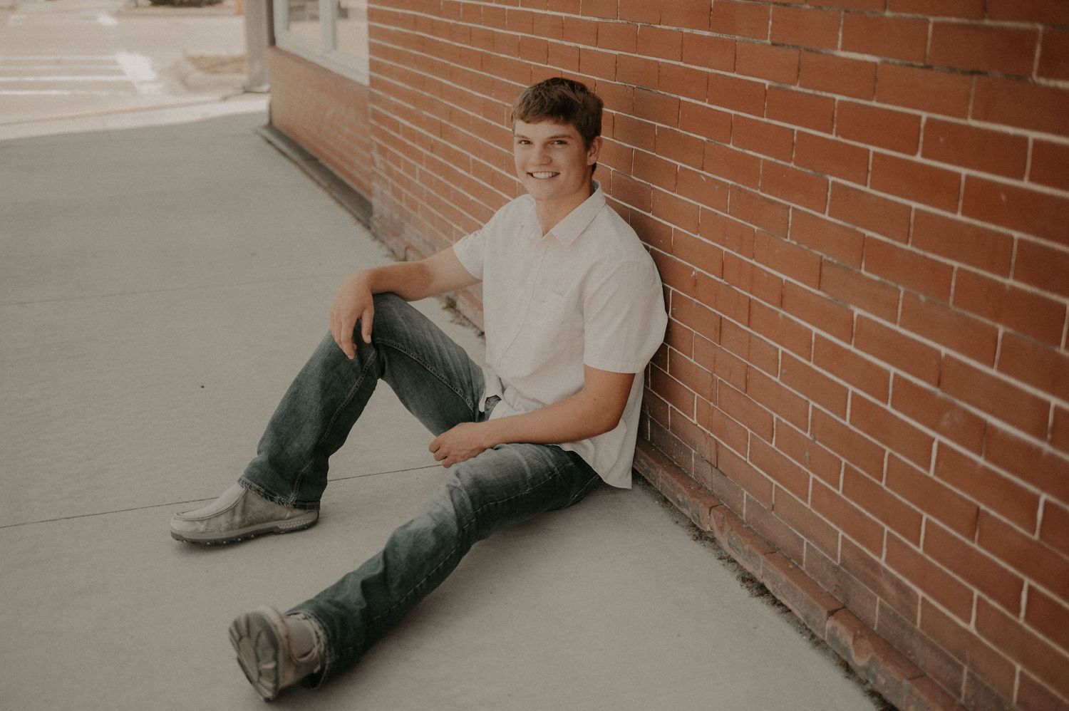Person in casual clothing sitting on concrete floor against brick wall in multiple sequential poses.