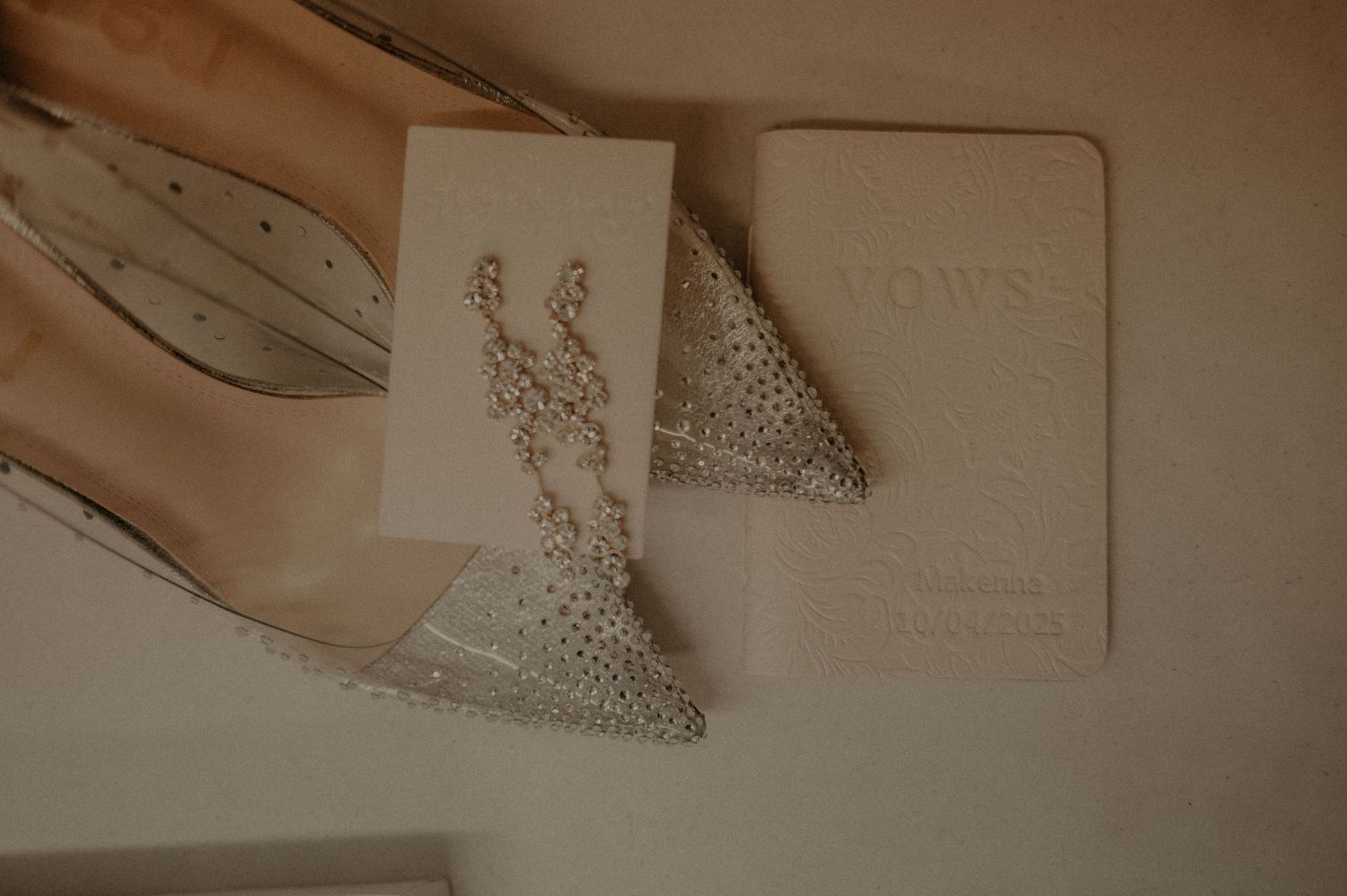 A wedding invitation suite with elegant calligraphy, rings, and blush pink details arranged on a neutral surface.