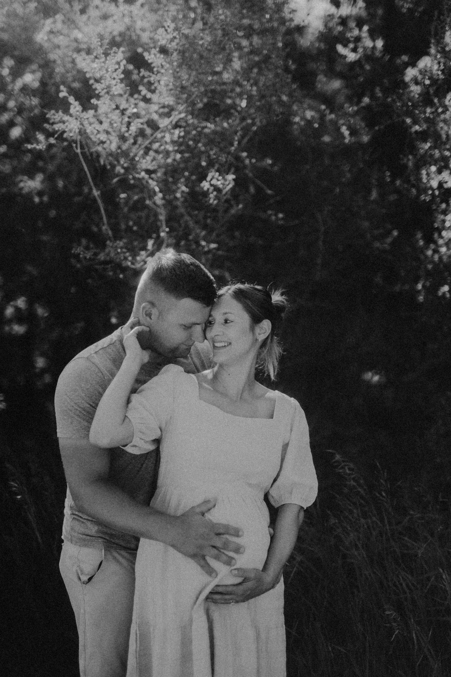 A romantic black and white maternity photoshoot featuring an intimate couple embracing outdoors.