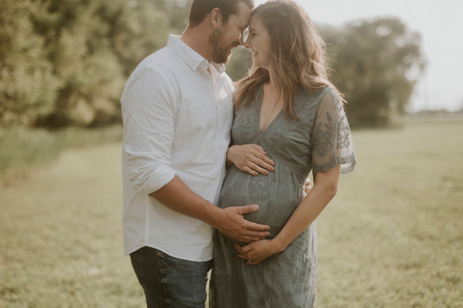 A couple shares tender moments in a sunlit meadow wearing coordinated white and sage green outfits.