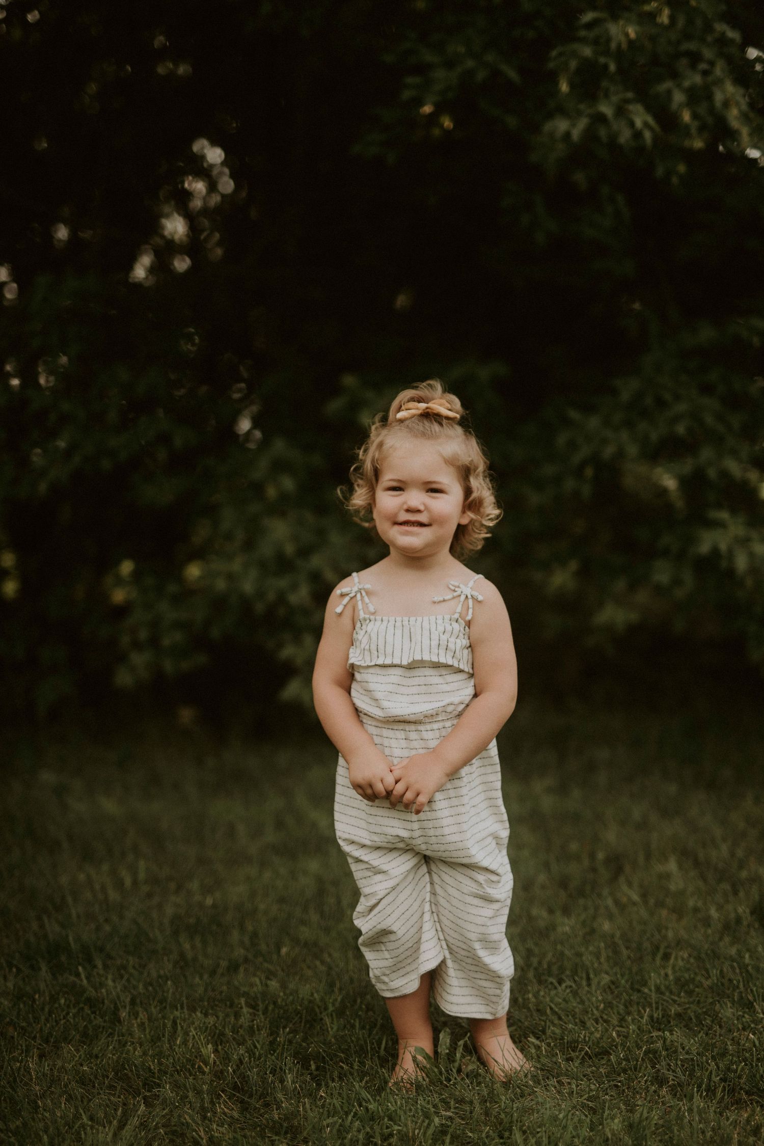 A series of outdoor portraits showing a small child in a light-colored striped outfit playing in grass.