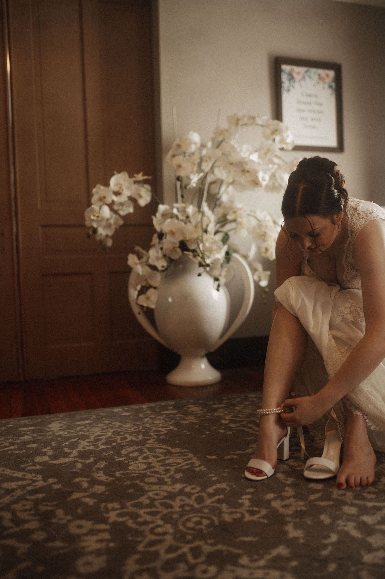A close-up view of someone adjusting their shoes on a patterned carpet with white floral decorations in the background.