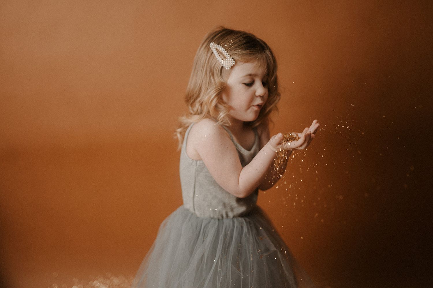 Child's hands playing with sparkly glitter scattered on a warm brown surface in moody lighting.