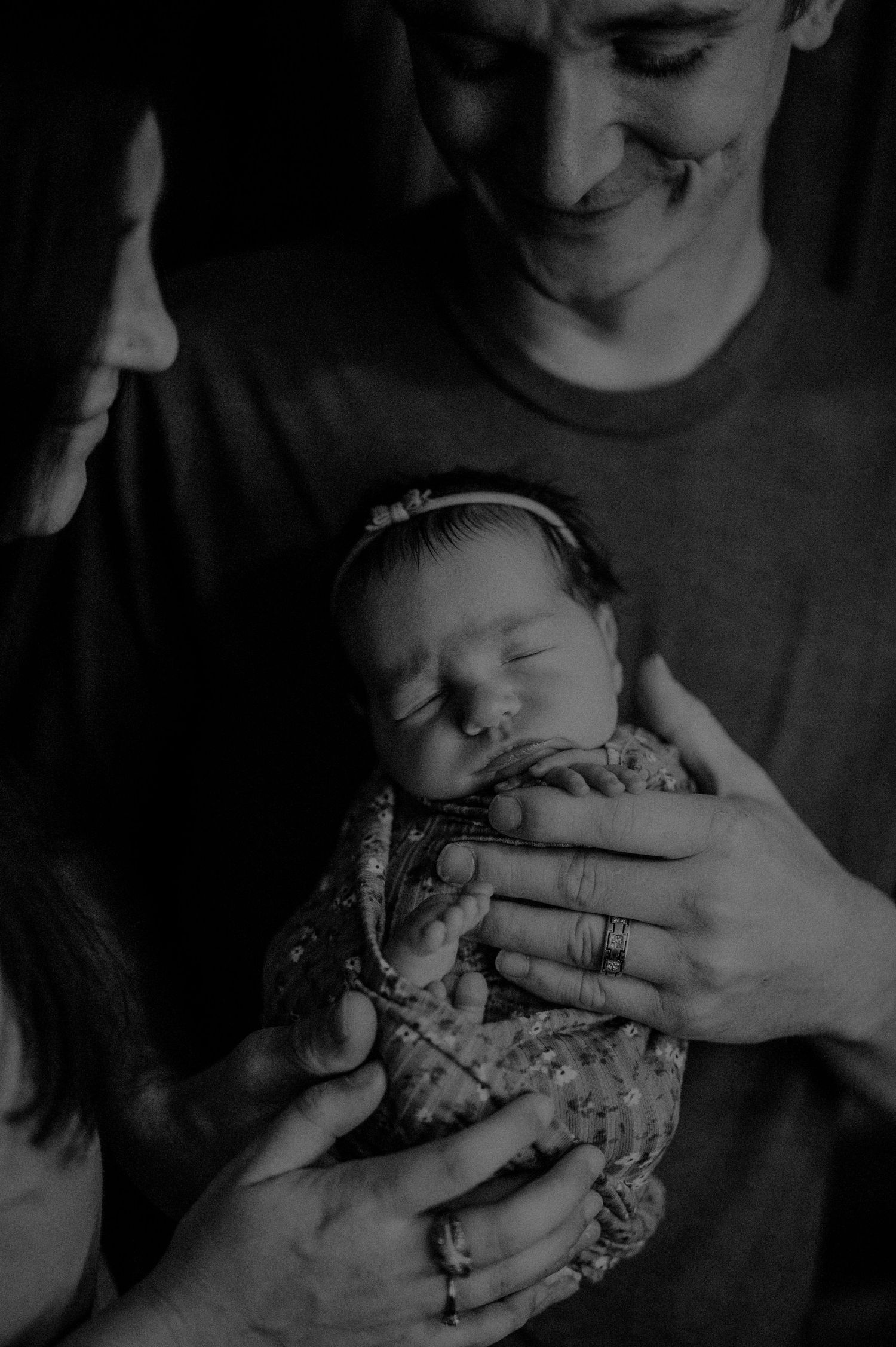 Black and white close-up photo of a sleeping newborn baby being cradled in gentle hands.