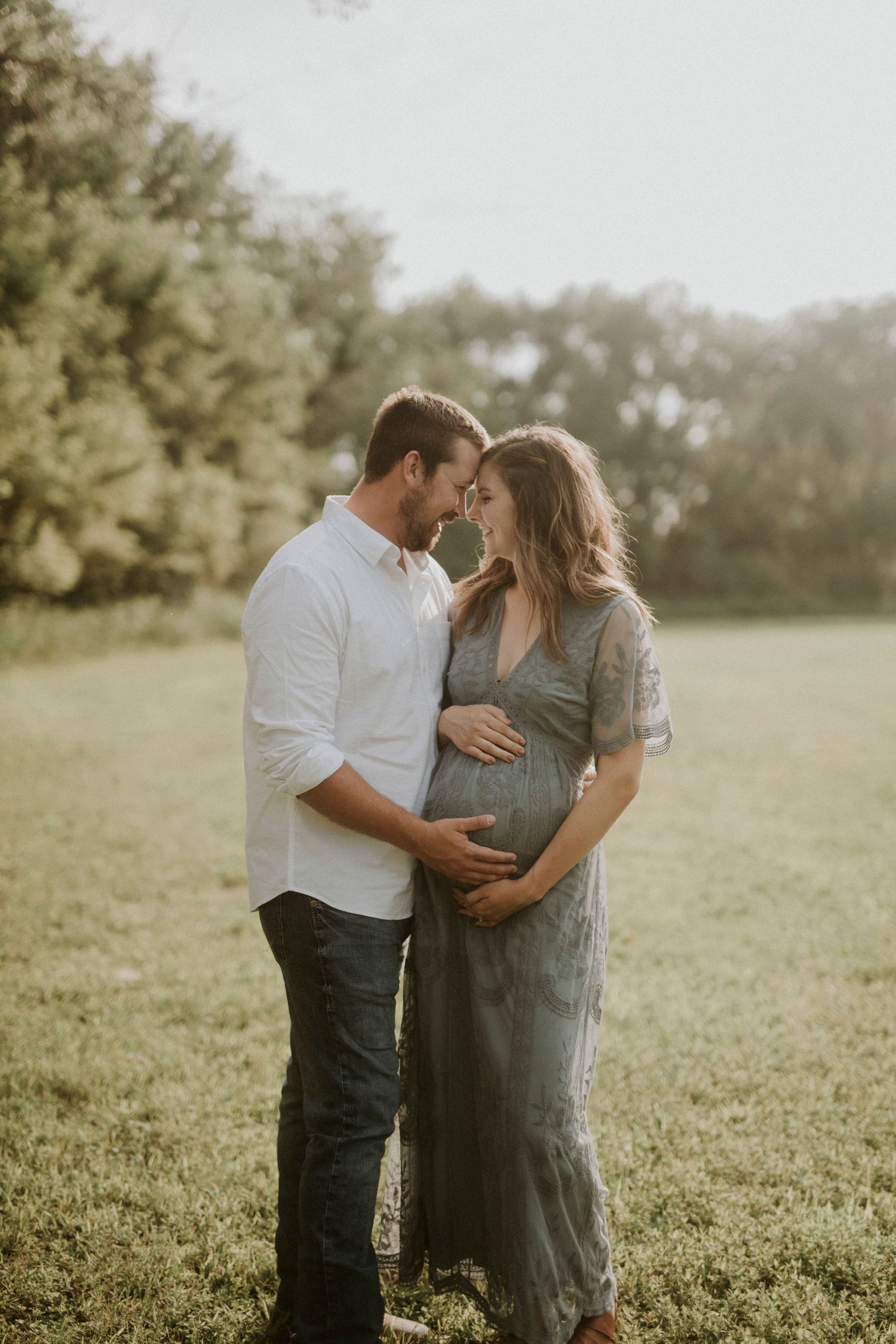 A couple shares an intimate moment together in a sunlit field surrounded by lush greenery.