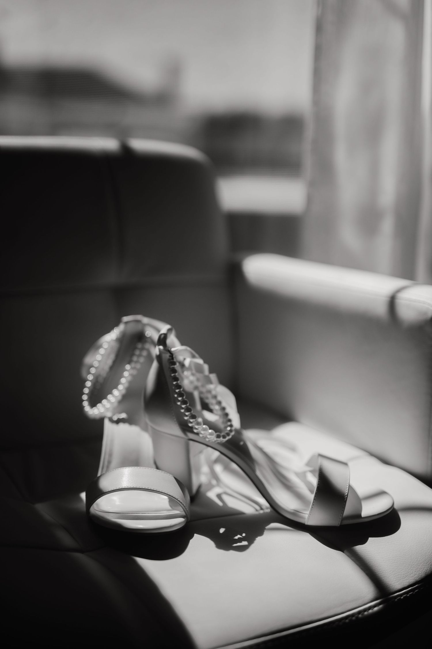 Black and white photo of delicate wedding sandals on leather surface.