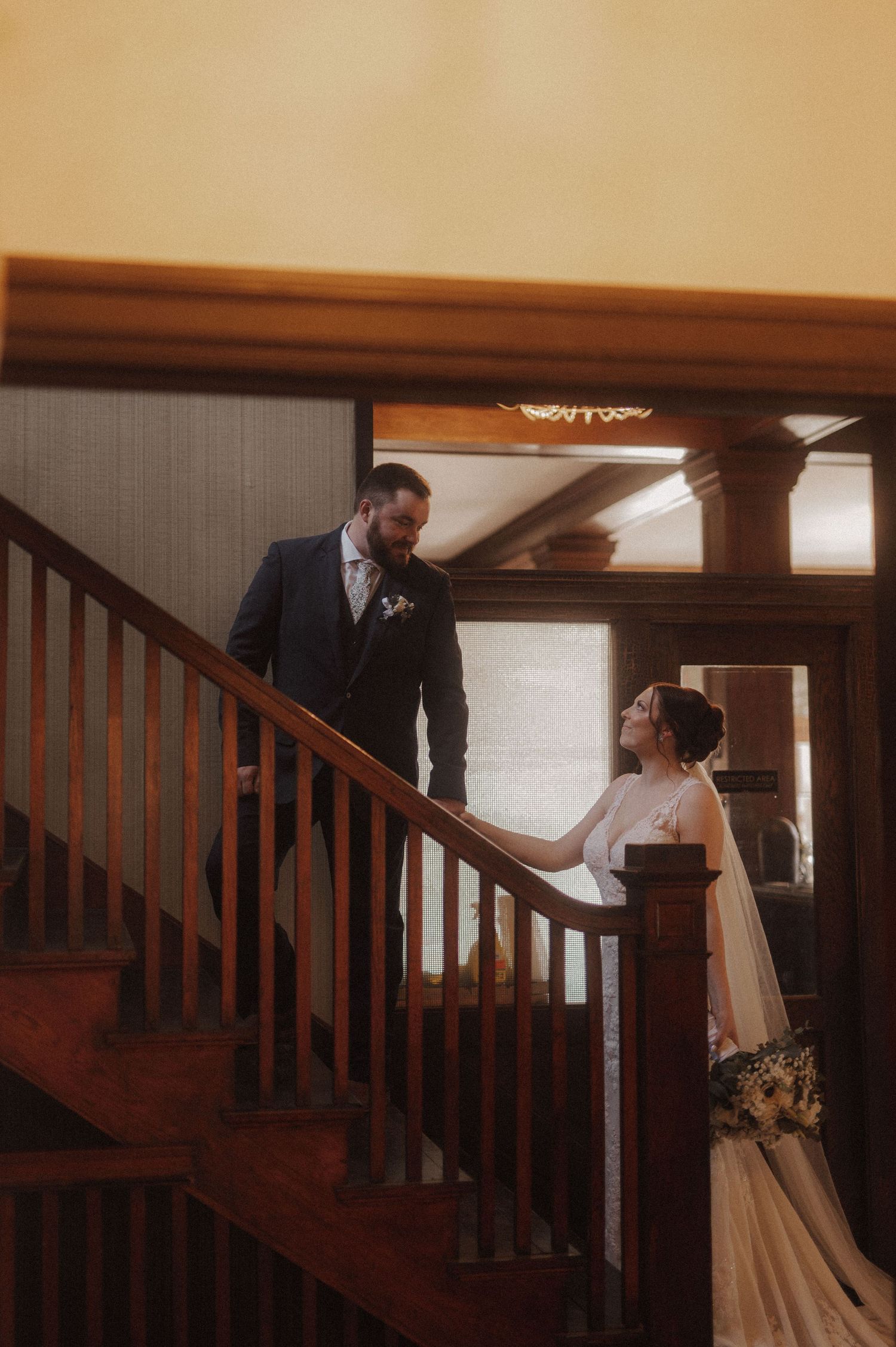 A wedding couple shares a tender moment on an elegant wooden staircase.