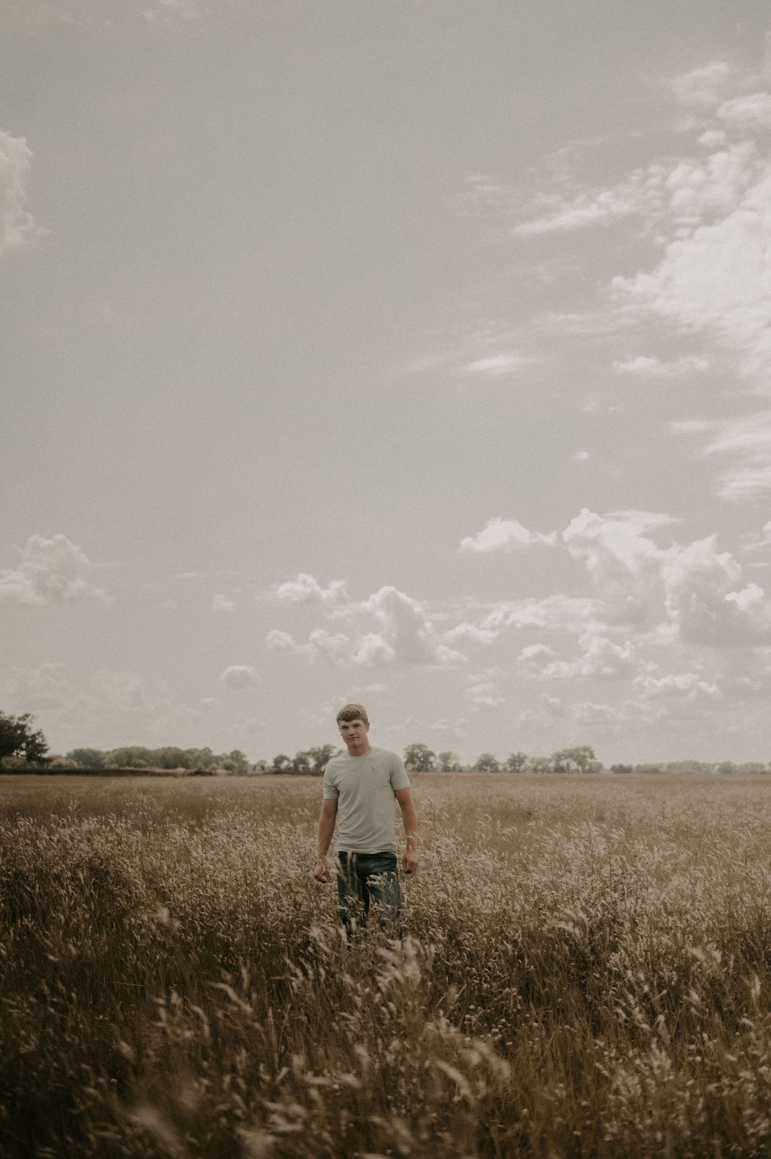 A person stands in a vast golden wheat field under a cloudy sky during sunset.