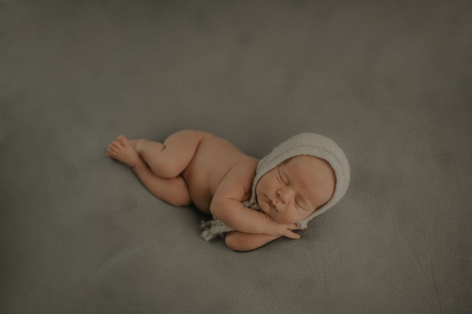 Peaceful newborn baby resting on grey backdrop in minimalist portrait style.