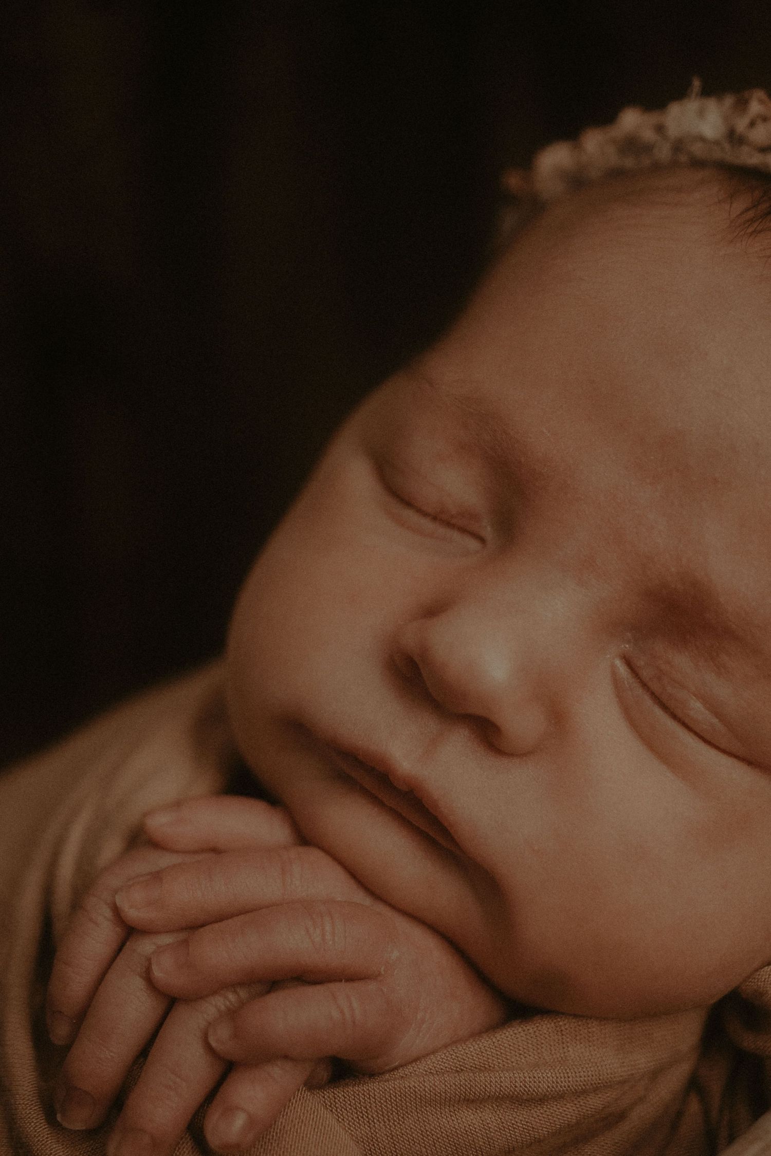Close-up sepia portrait of a newborn baby sleeping with hand near face.