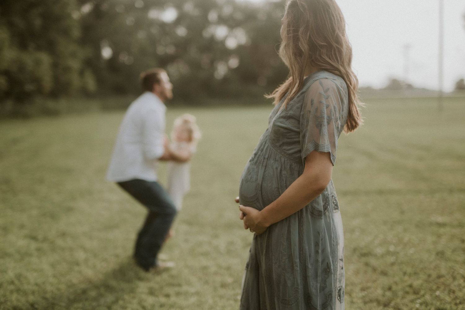 A couple embraces in a serene green field during a romantic outdoor photo session.