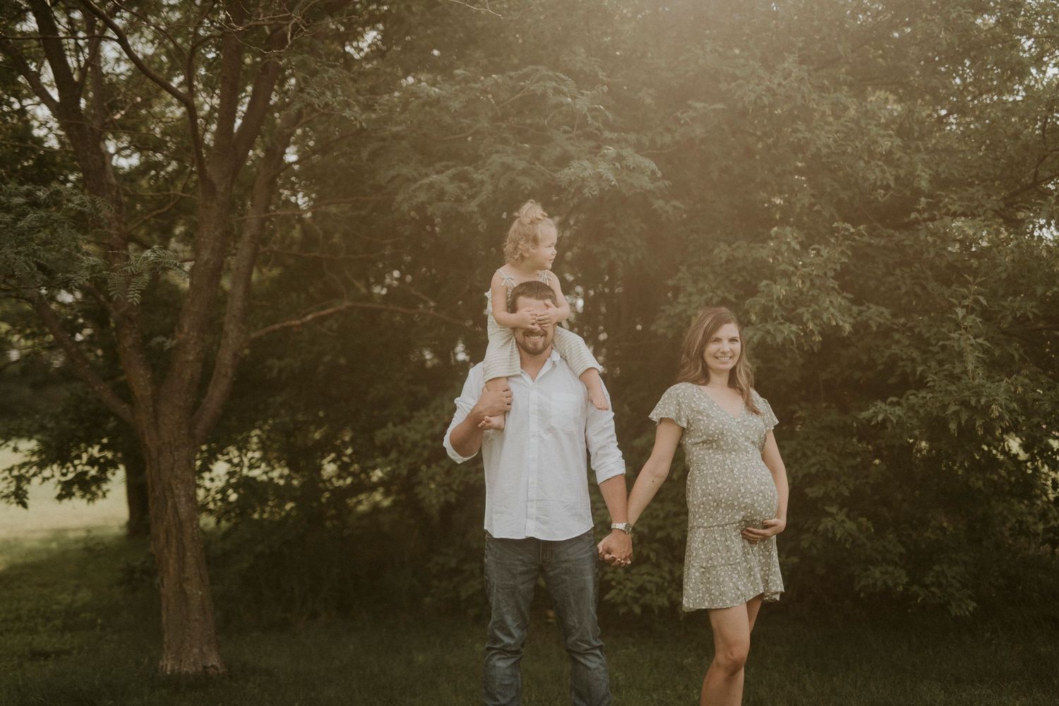 Family walks together through a sunlit park path during golden hour creating beautiful silhouettes against trees.