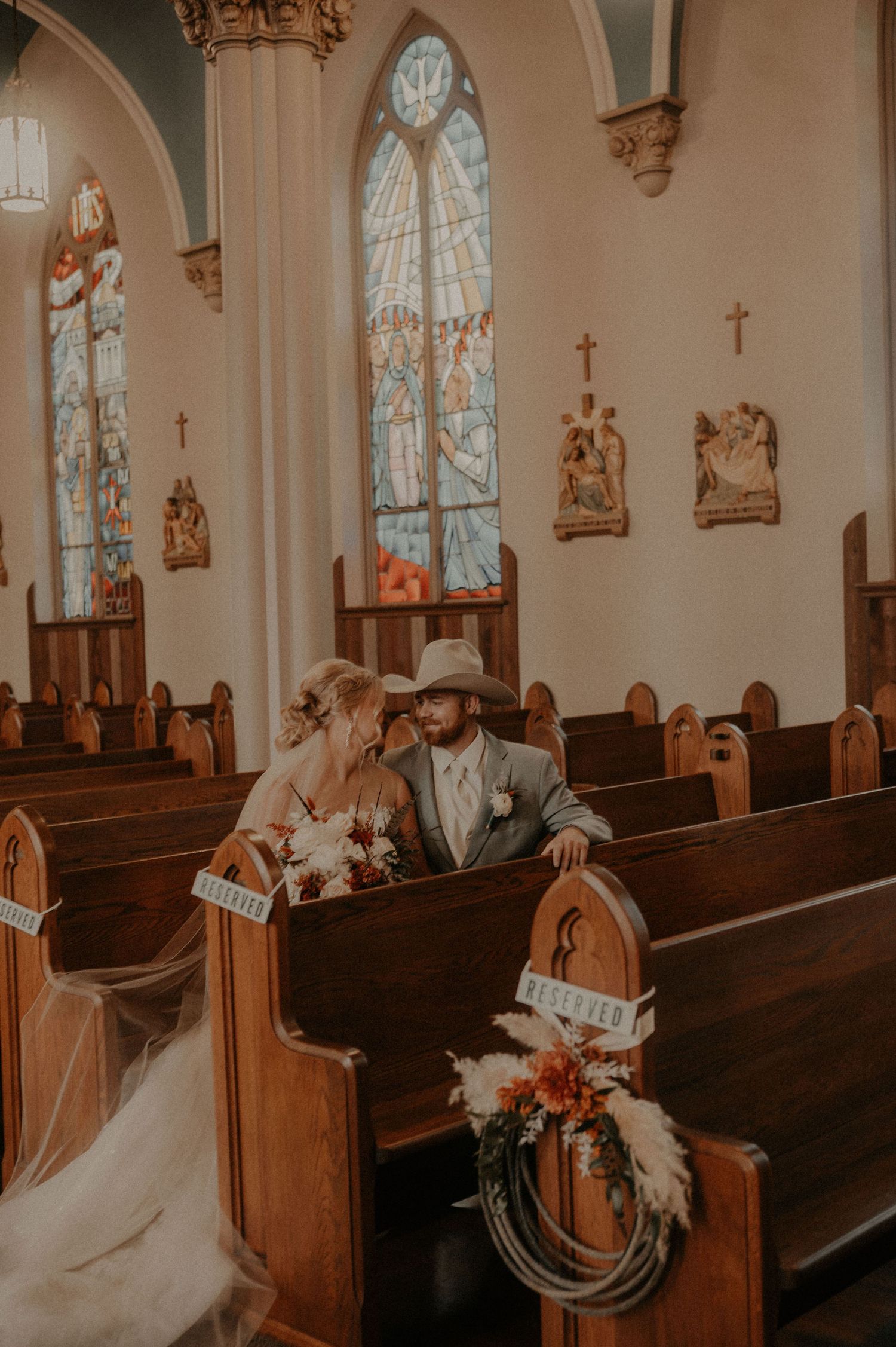 A couple shares an intimate moment in a church pew with stained glass windows and ornate architecture in the background.