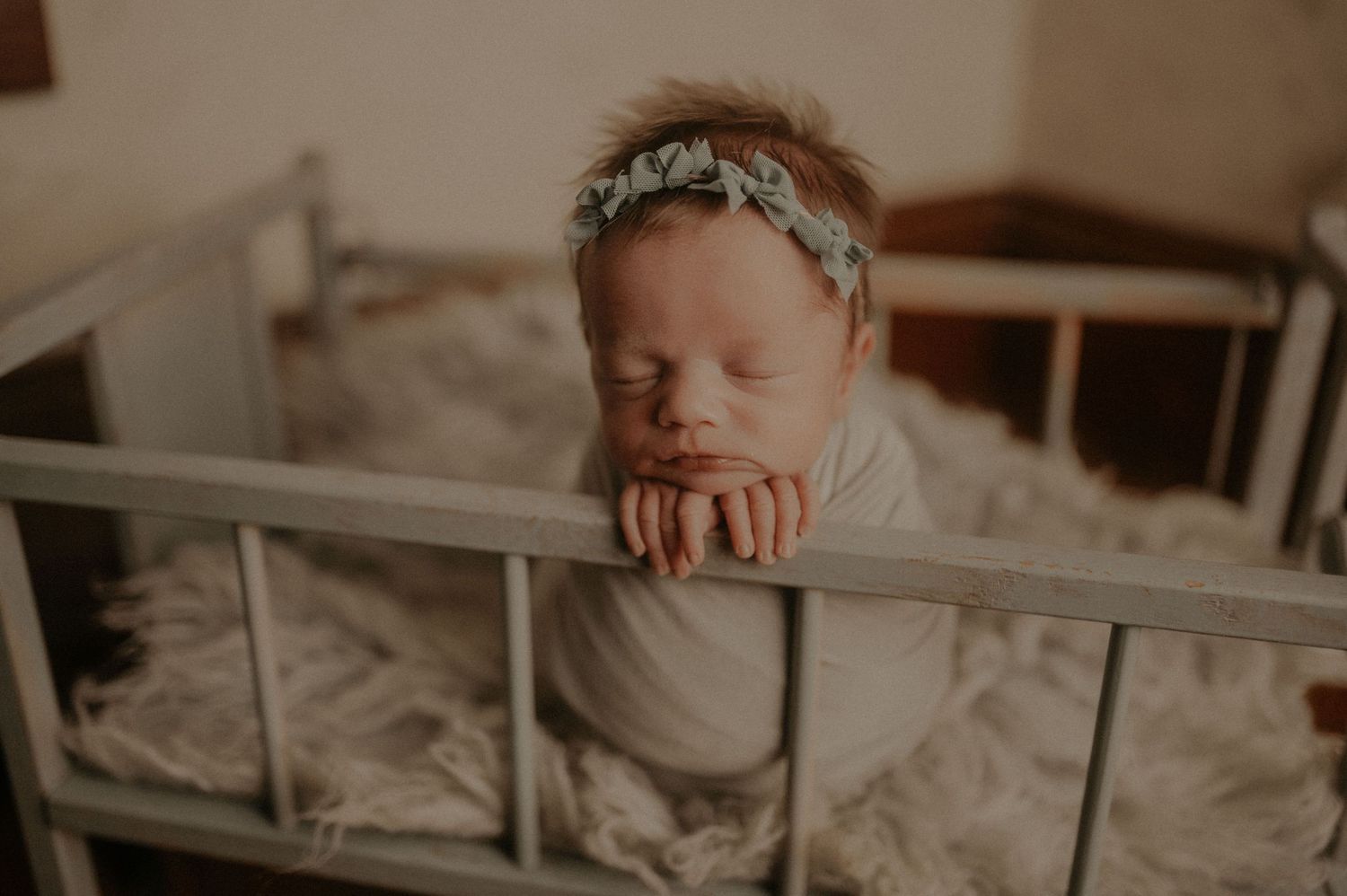 Newborn baby sleeping peacefully on soft white textured blanket in natural lighting.
