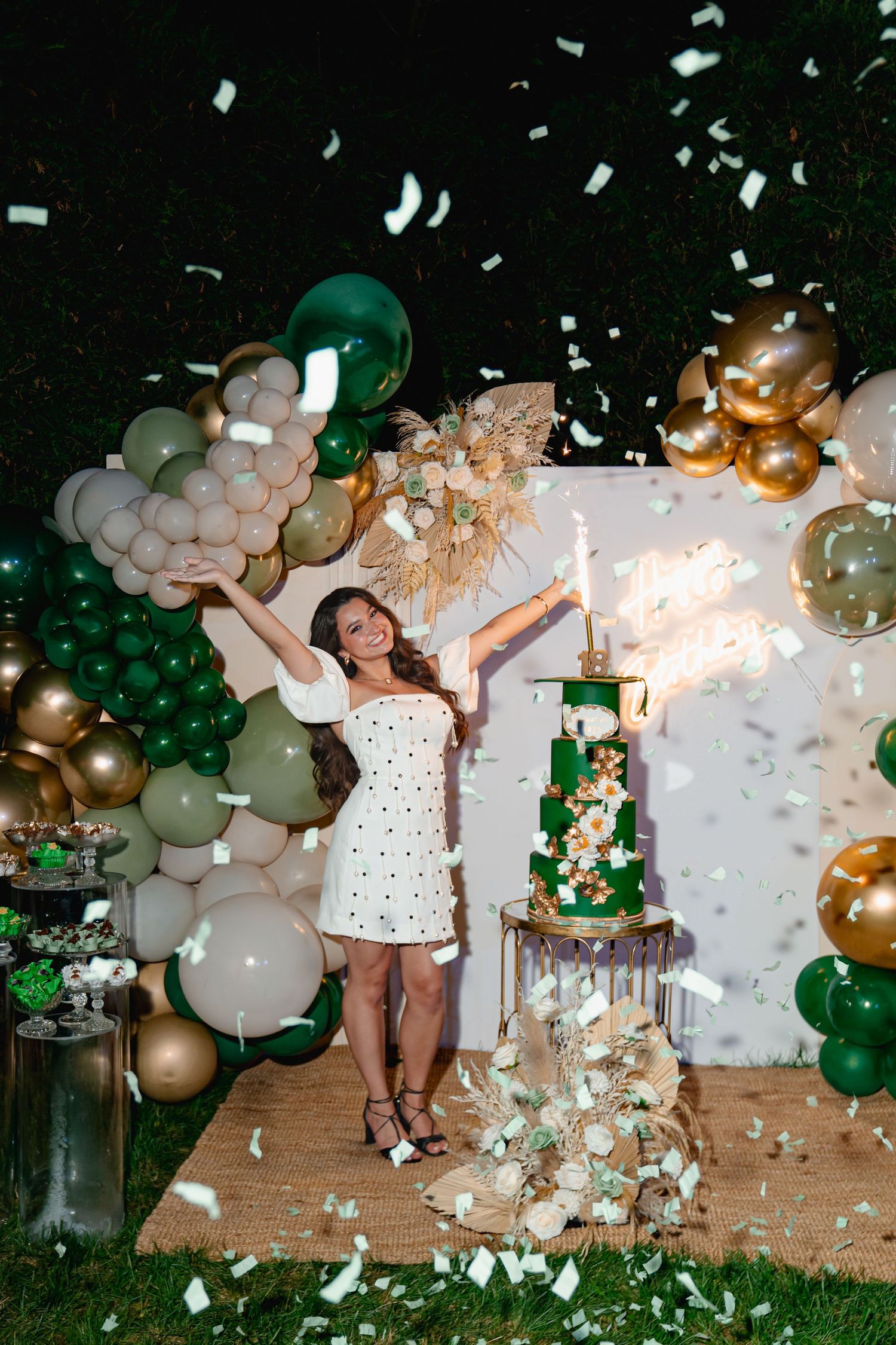 A celebratory scene with confetti flying through the air against a backdrop of green and gold balloon decorations. Boston MA photographer.