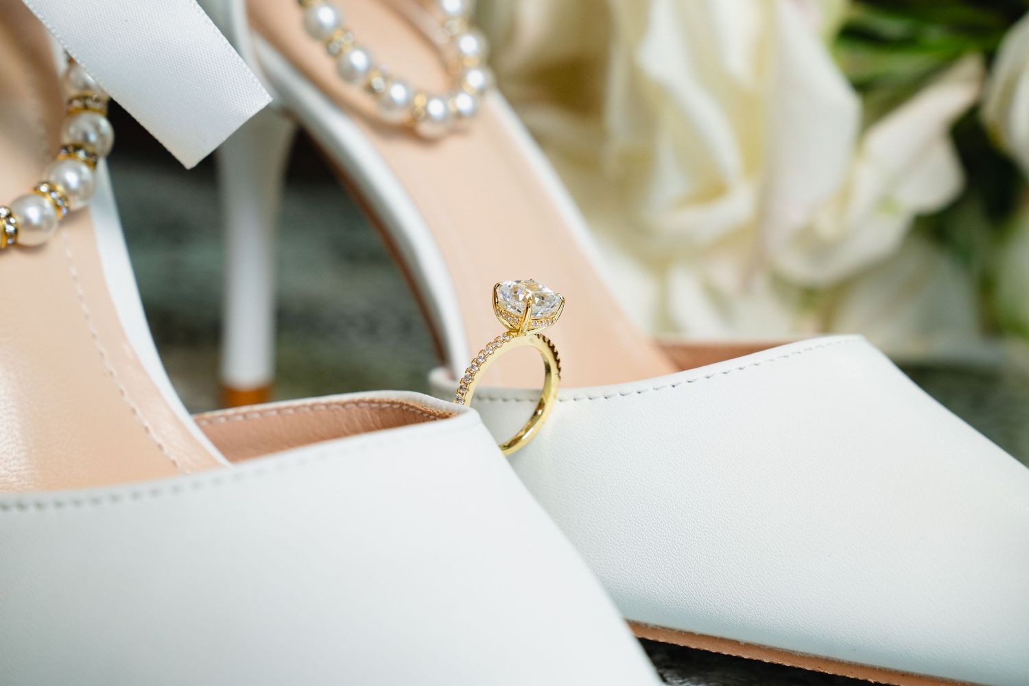 Elegant white bridal shoes with pearl and crystal embellishments displayed against floral wedding decor background. Boston MA photographer.