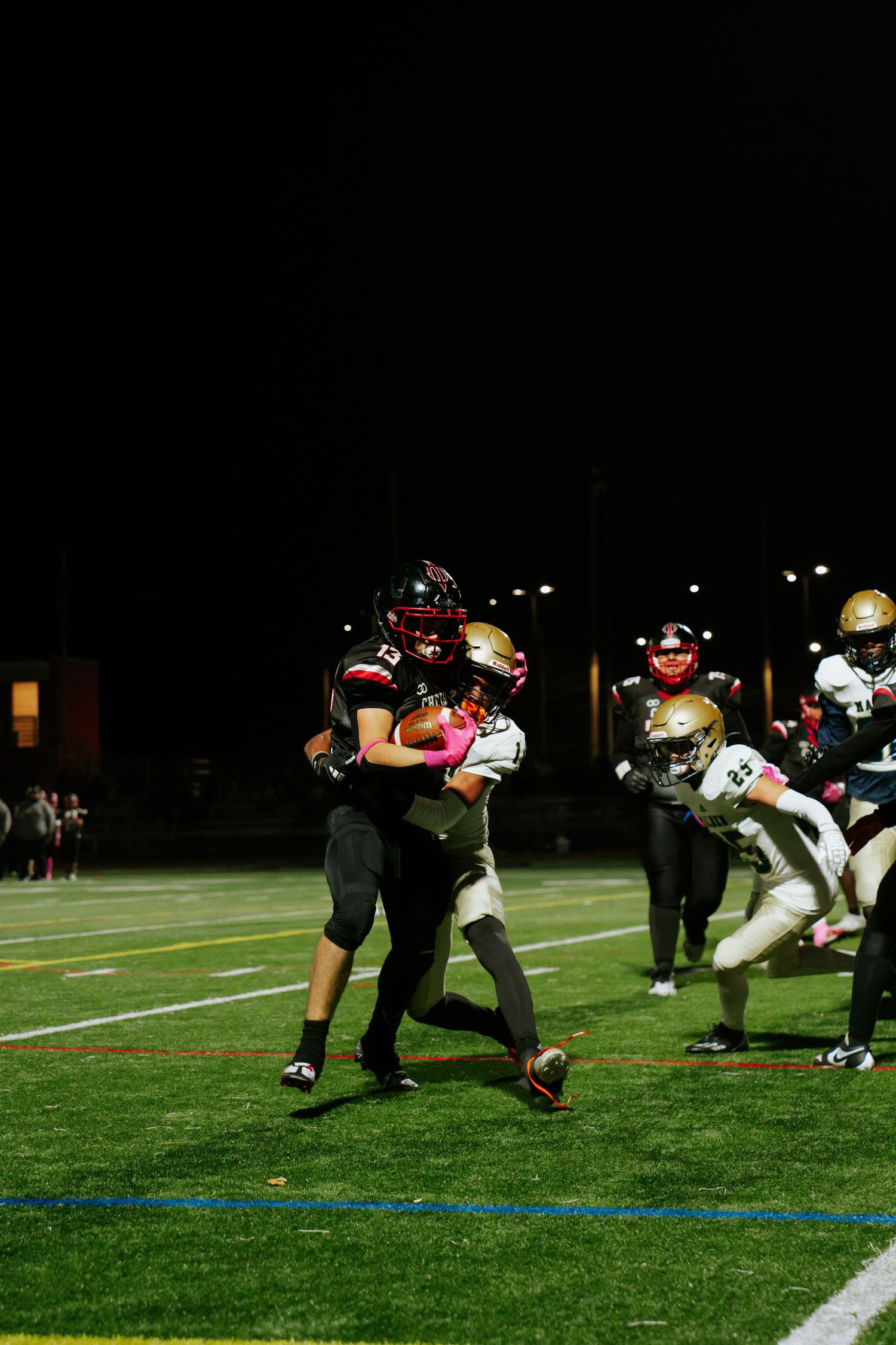 High school football players engage in a defensive play during a nighttime game on an illuminated field. Boston MA photographer, Malden MA.