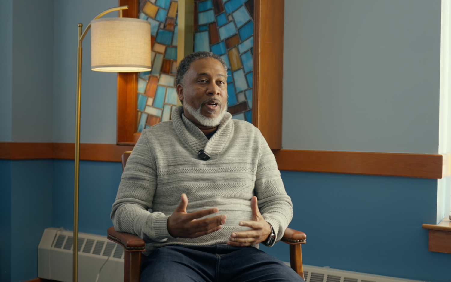 A person in a gray sweater sits on a couch while using for a professional video. Boston MA photographer, Malden MA and Greater Boston.