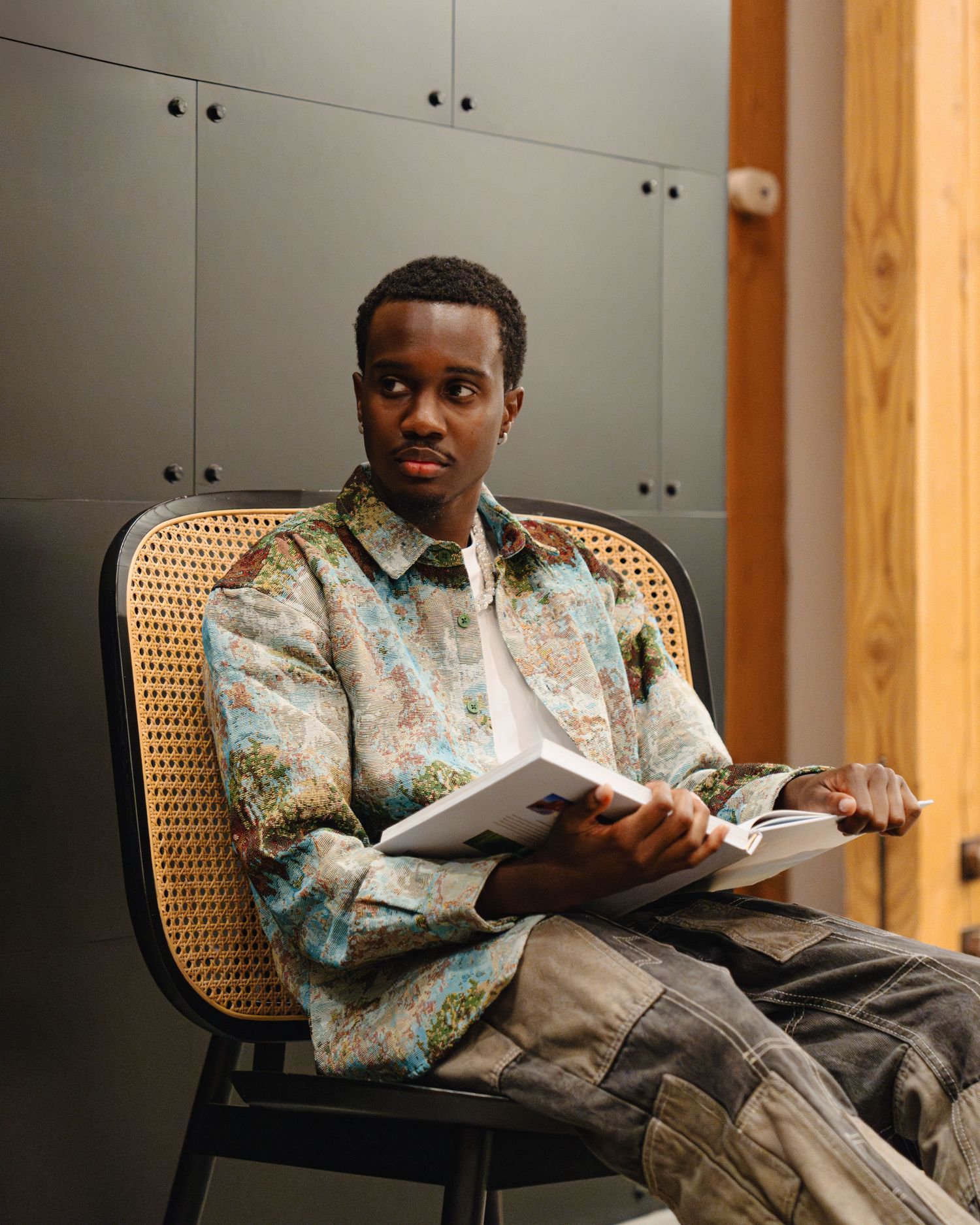 A person in a floral print shirt sits comfortably in a cane back chair while reading through papers. Boston MA photographer, Malden MA.