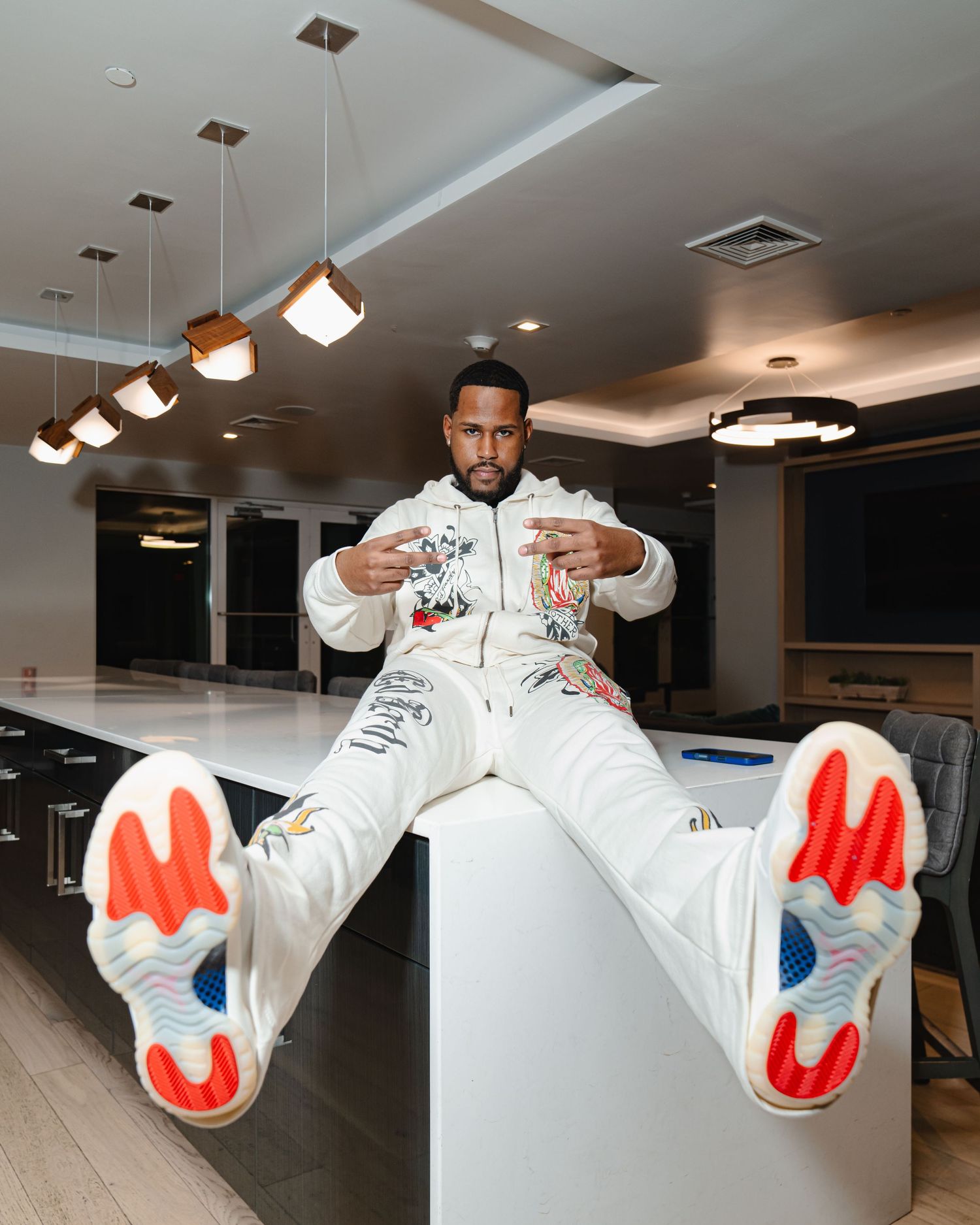 Person in white patterned tracksuit performs dynamic poses in modern interior space with pendant lighting. Greater Boston Area photographer.