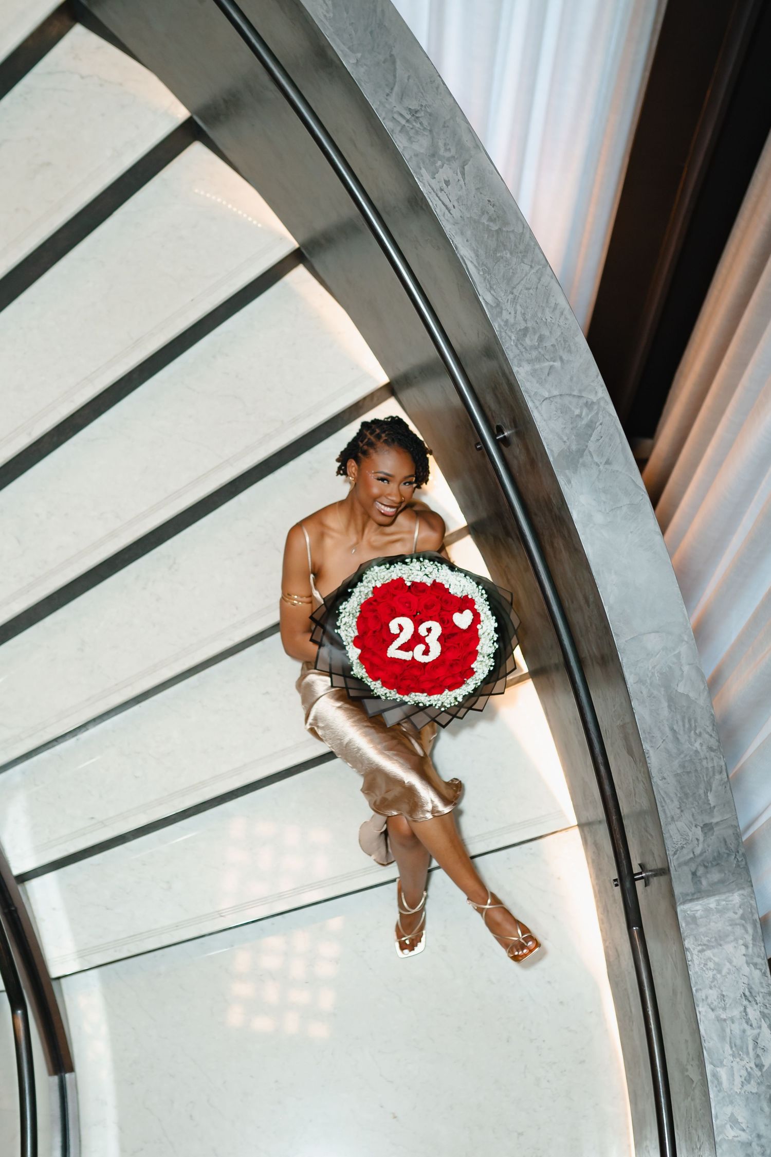 Overhead view of curved staircase with person in formal dress holding decorative number. Greater Boston Area photographer, Malden MA.